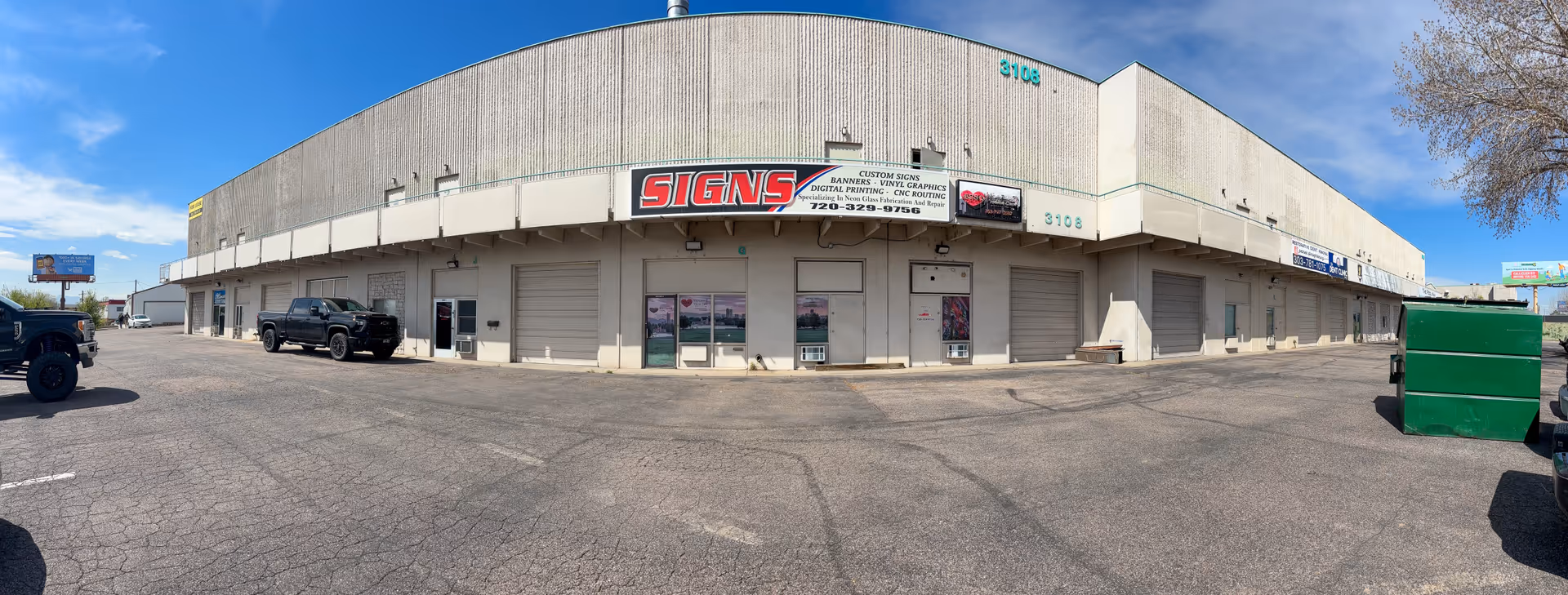Wide exterior view of a beige commercial building with signs and loading bays.