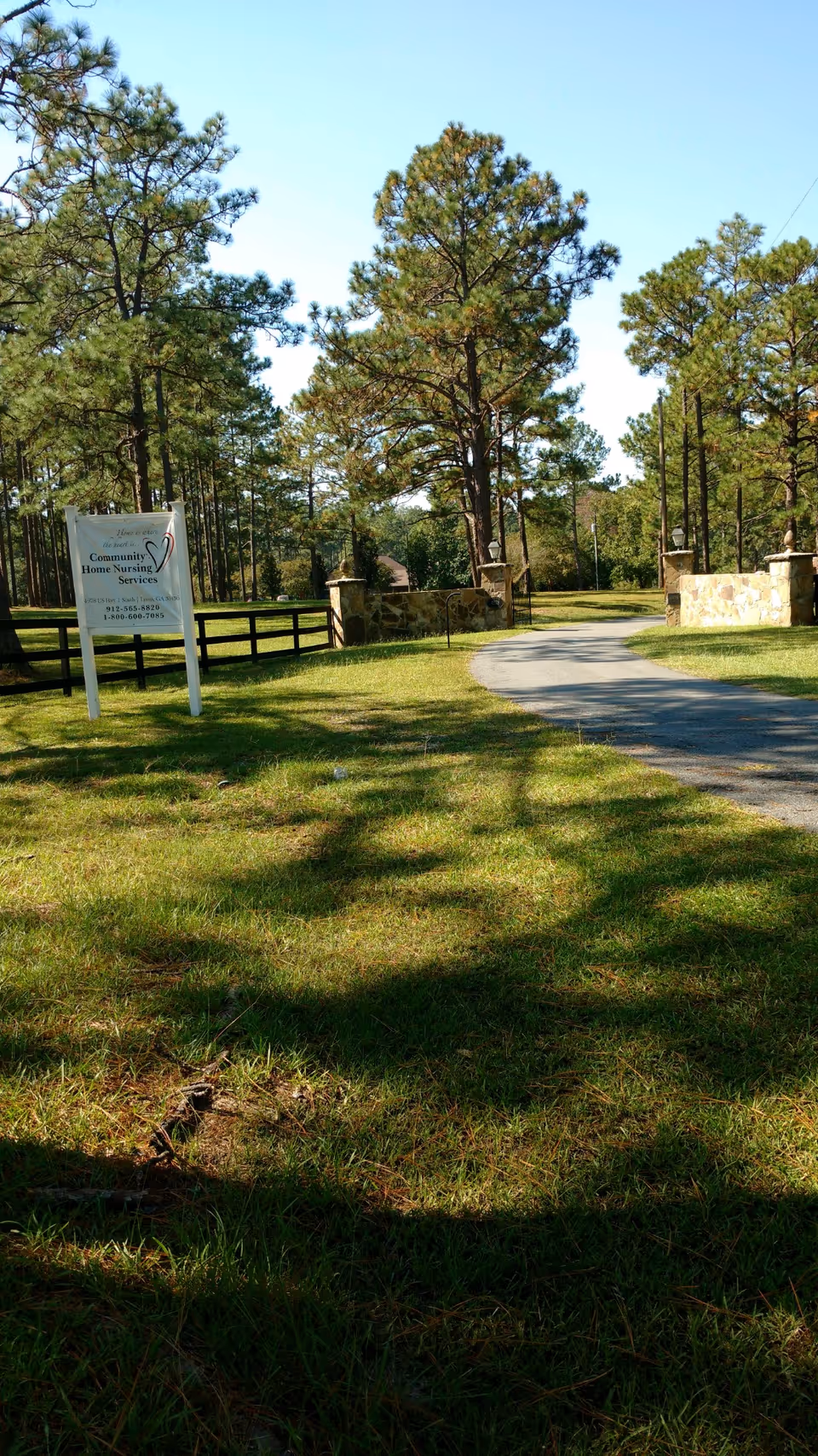 Outdoor view of a grassy entrance with a sign for Community Home Nursing Services and trees.