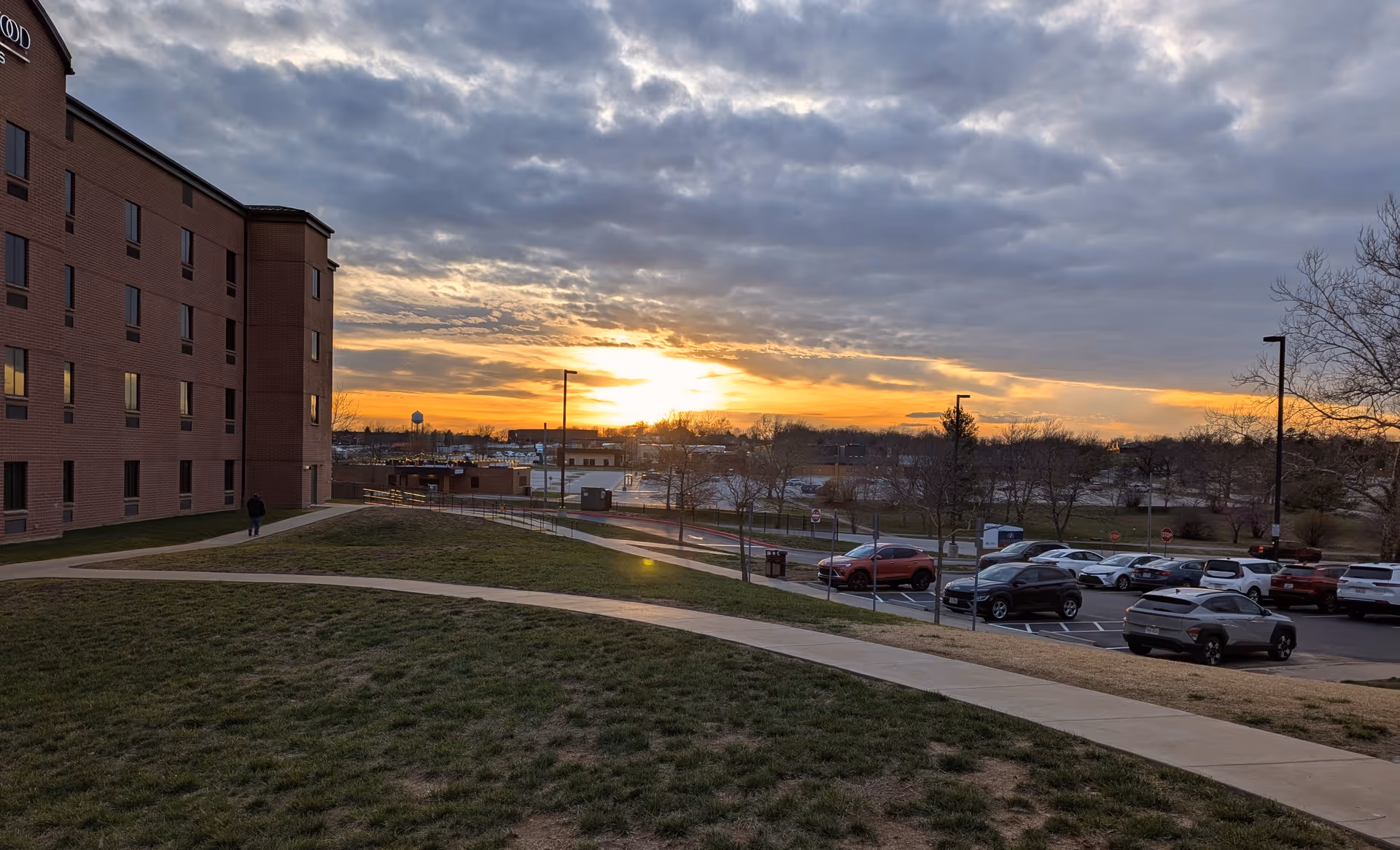 Sunset over a brick senior living building with a curved walkway and parking lot.