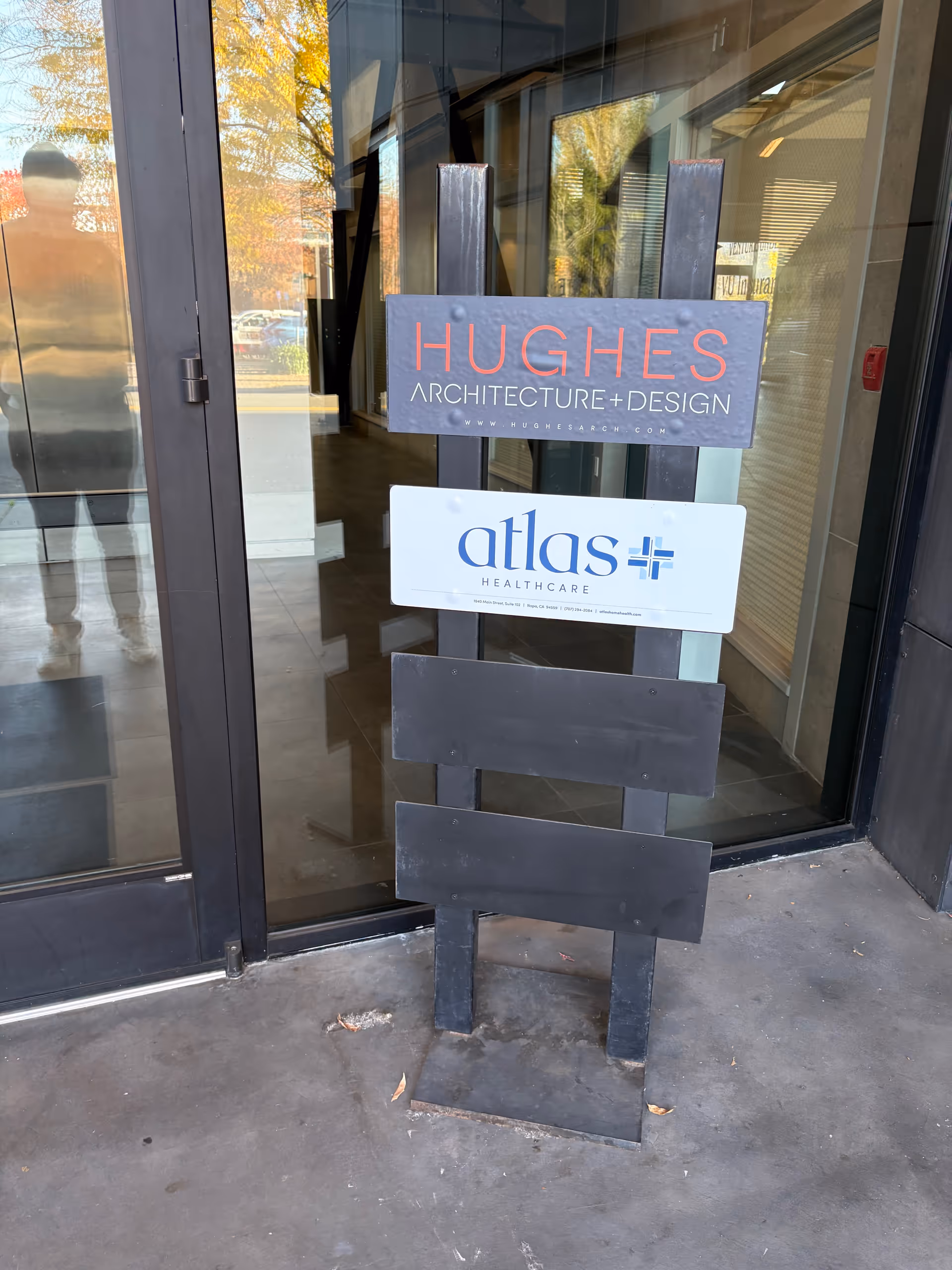 Exterior entrance with a signboard displaying Hughes Architecture and Design, and an Atlas Healthcare sign.