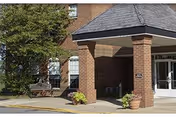 Exterior entrance of a brick senior living facility with a covered entry and potted plants.
