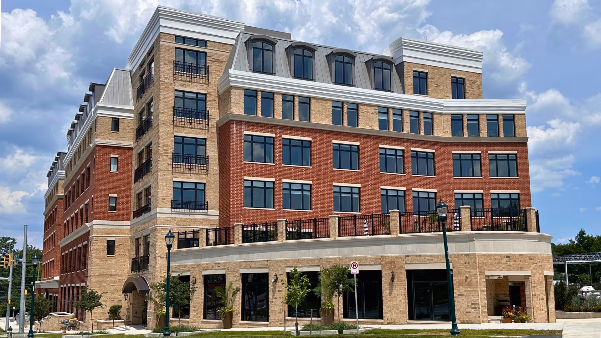 A multi-story brick senior living building with balconies and large windows along a curved street.