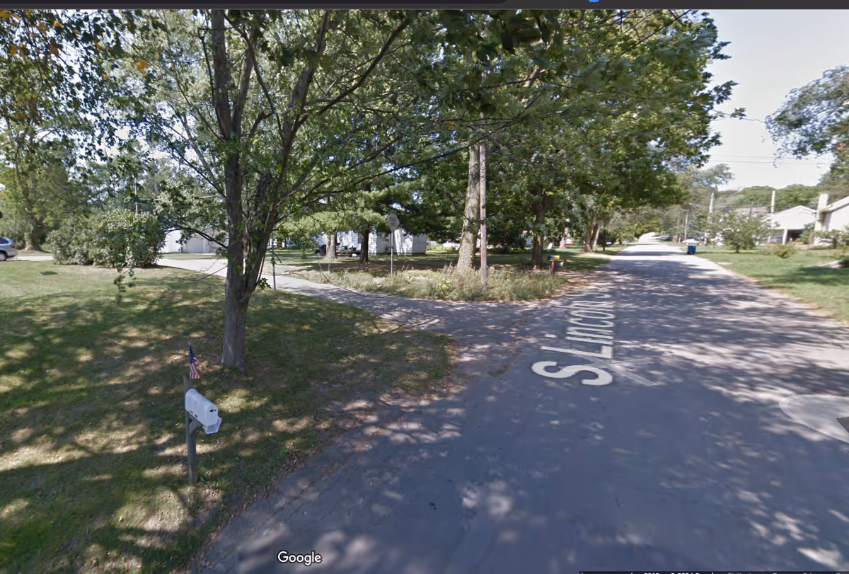 Tree-lined street with a mailbox and parked homes along a quiet road.