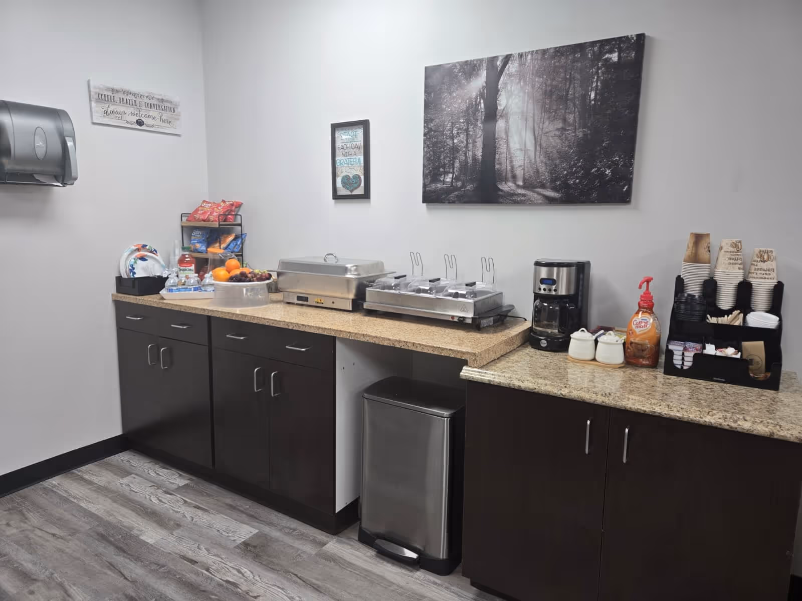 Service counter with chafing dishes, coffee maker, cups, fruit, and snacks in a facility kitchen.
