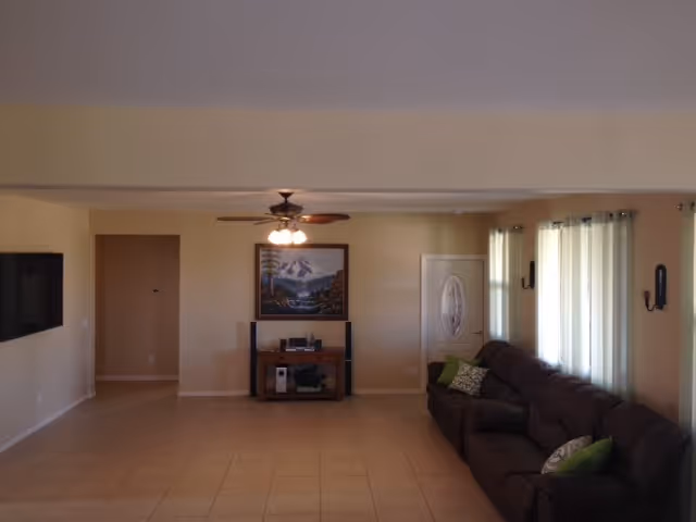 Spacious senior living room with beige walls, tile floor, ceiling fan, and sofa.