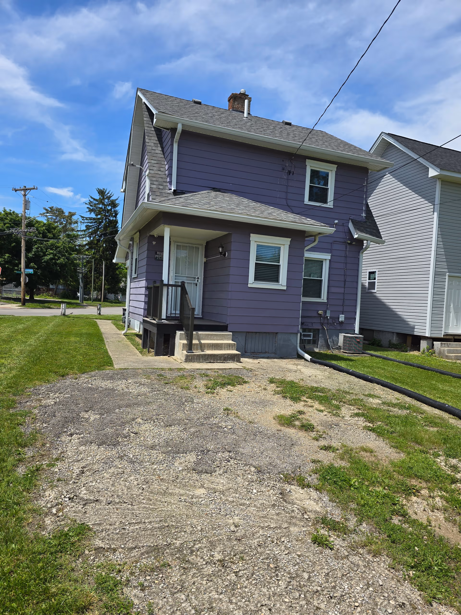 Purple two-story house with front steps and a gravel driveway under a blue sky.