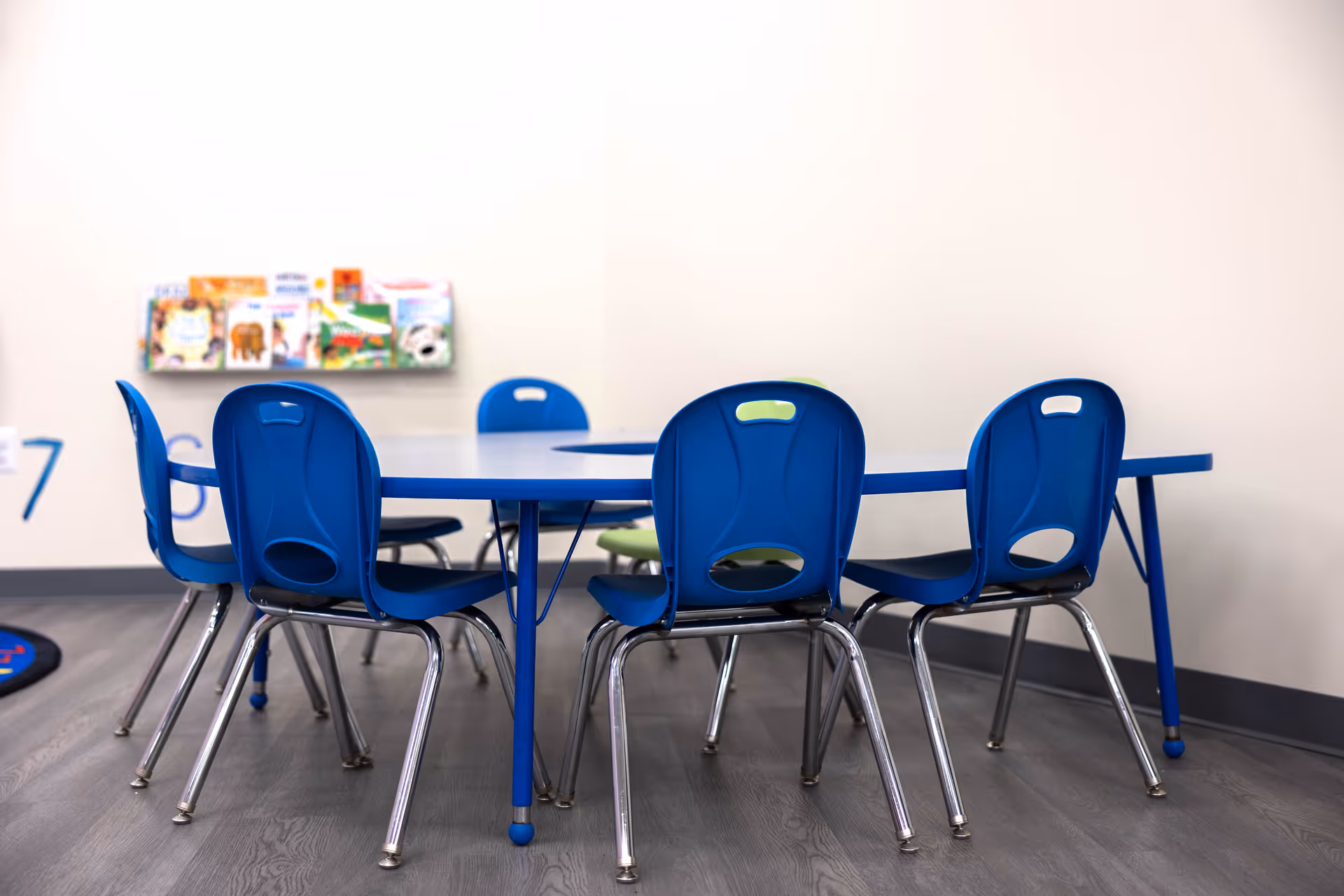 Blue plastic chairs surround a blue table in a bright children's activity room.