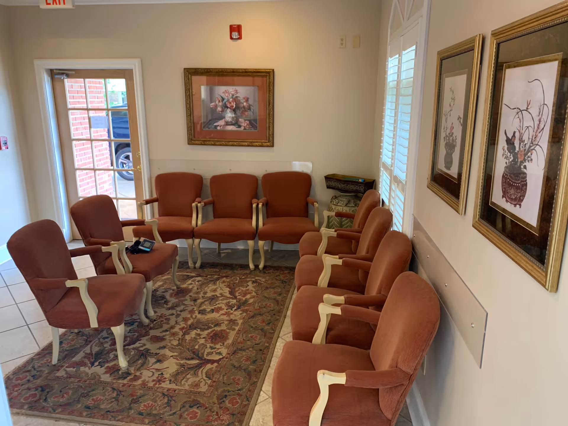 Beige-walled interior waiting area with red upholstered chairs and framed art.