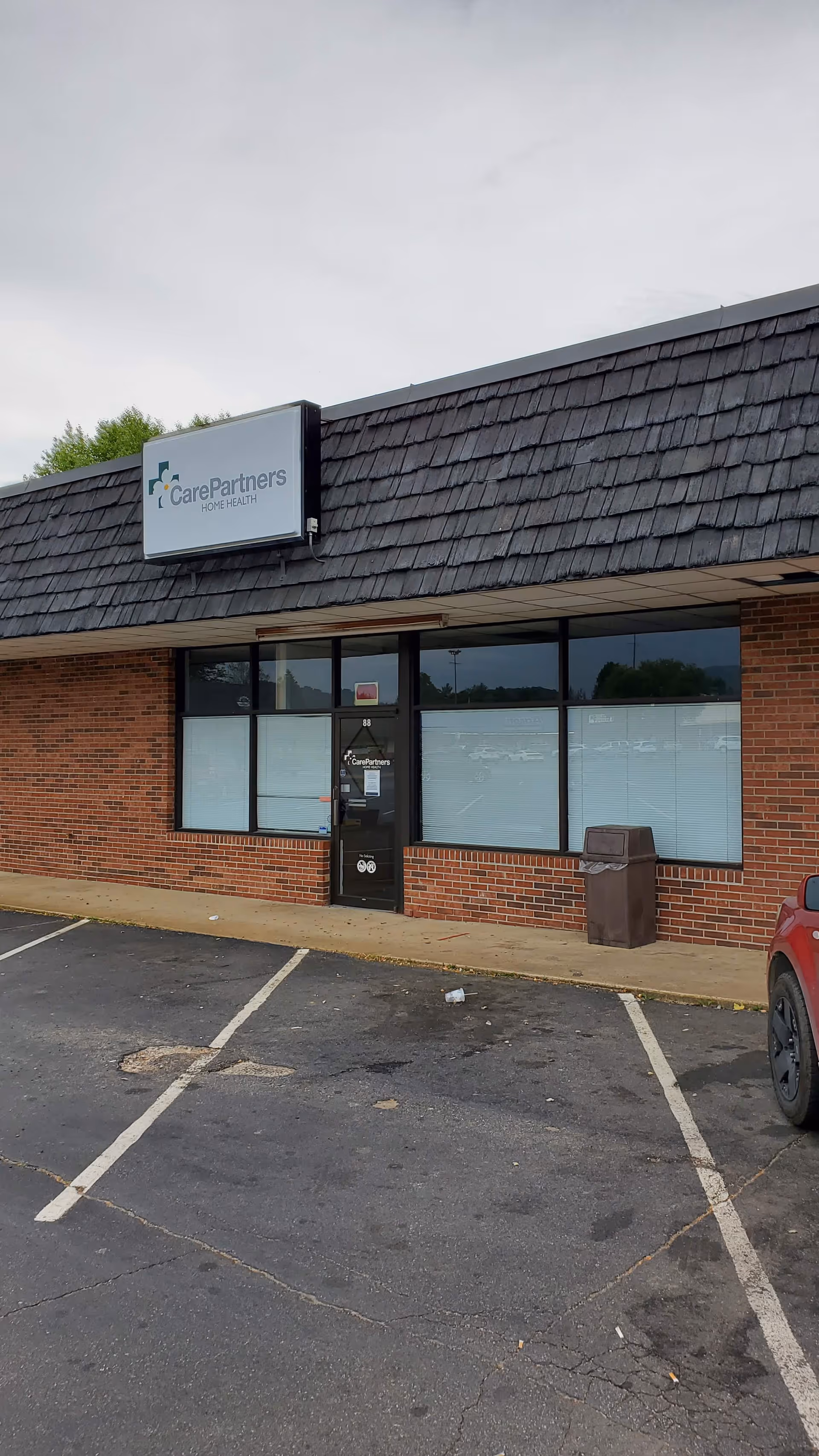 Brick exterior CarePartners Home Health building with sign and parking lot in front.