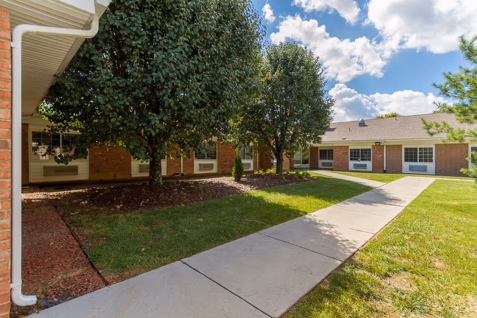 Exterior view of a brick senior living facility with walkway and trees.