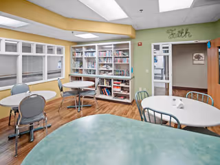 Interior common area of a senior living library with round tables and bookshelves.