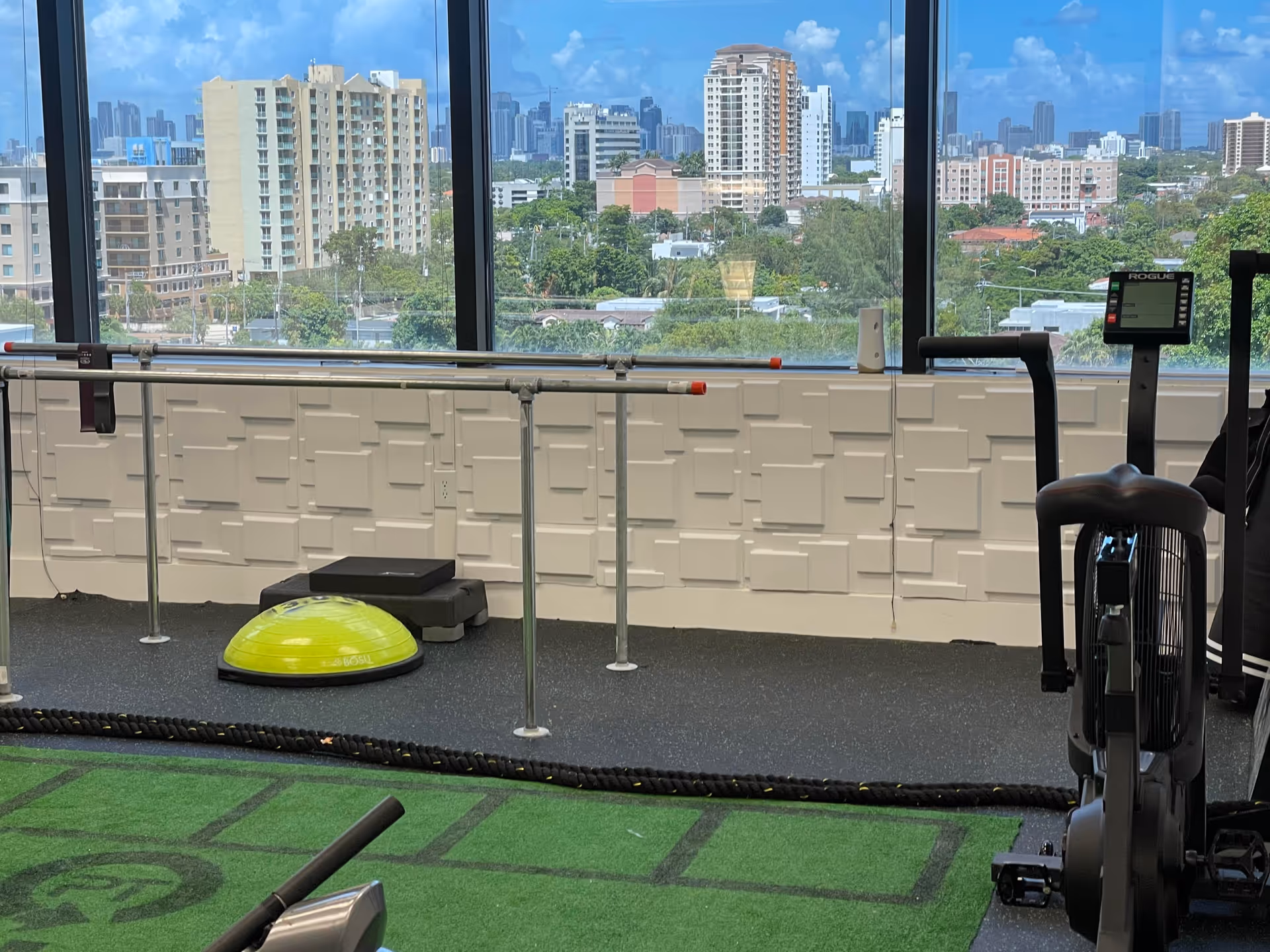 Gym area with exercise equipment and large windows overlooking a city skyline.