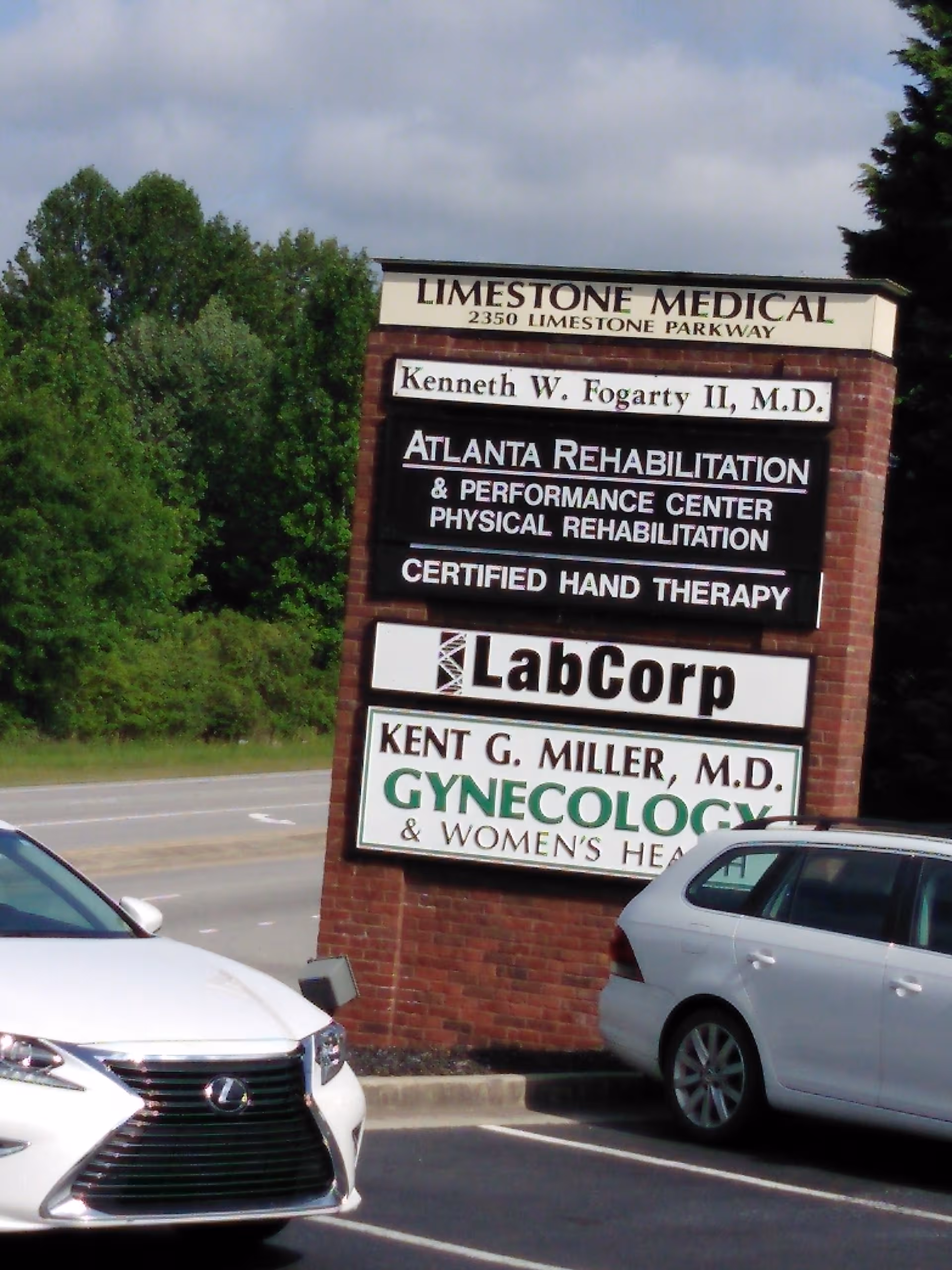 Outdoor brick sign advertising medical, rehabilitation, and lab services beside cars.