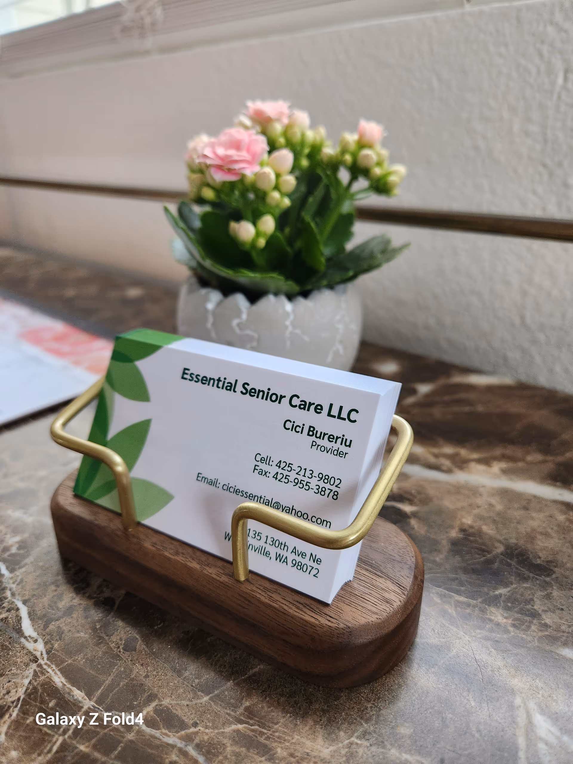 Business card for Essential Senior Care LLC in a wooden holder on a marble table.