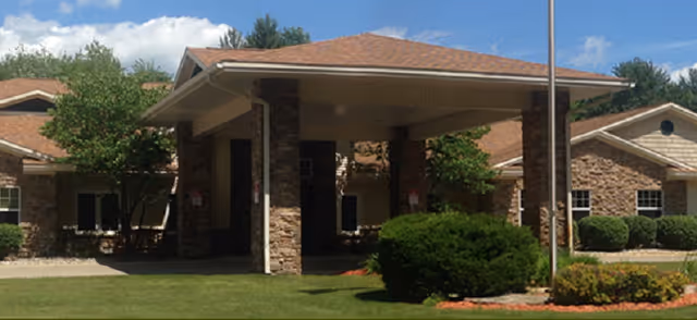 Exterior view of a senior living facility entrance with stone columns and landscaping.