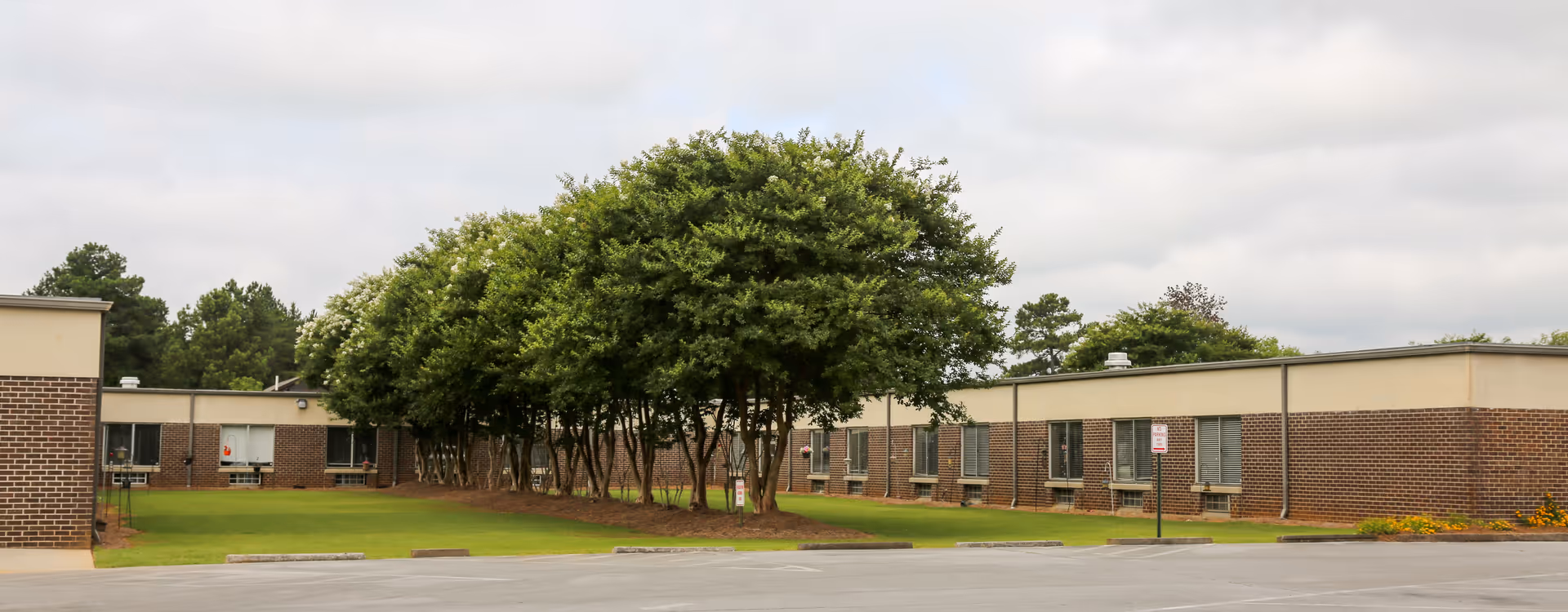 Single-story brick senior living facility with a grassy lawn and trees in front
