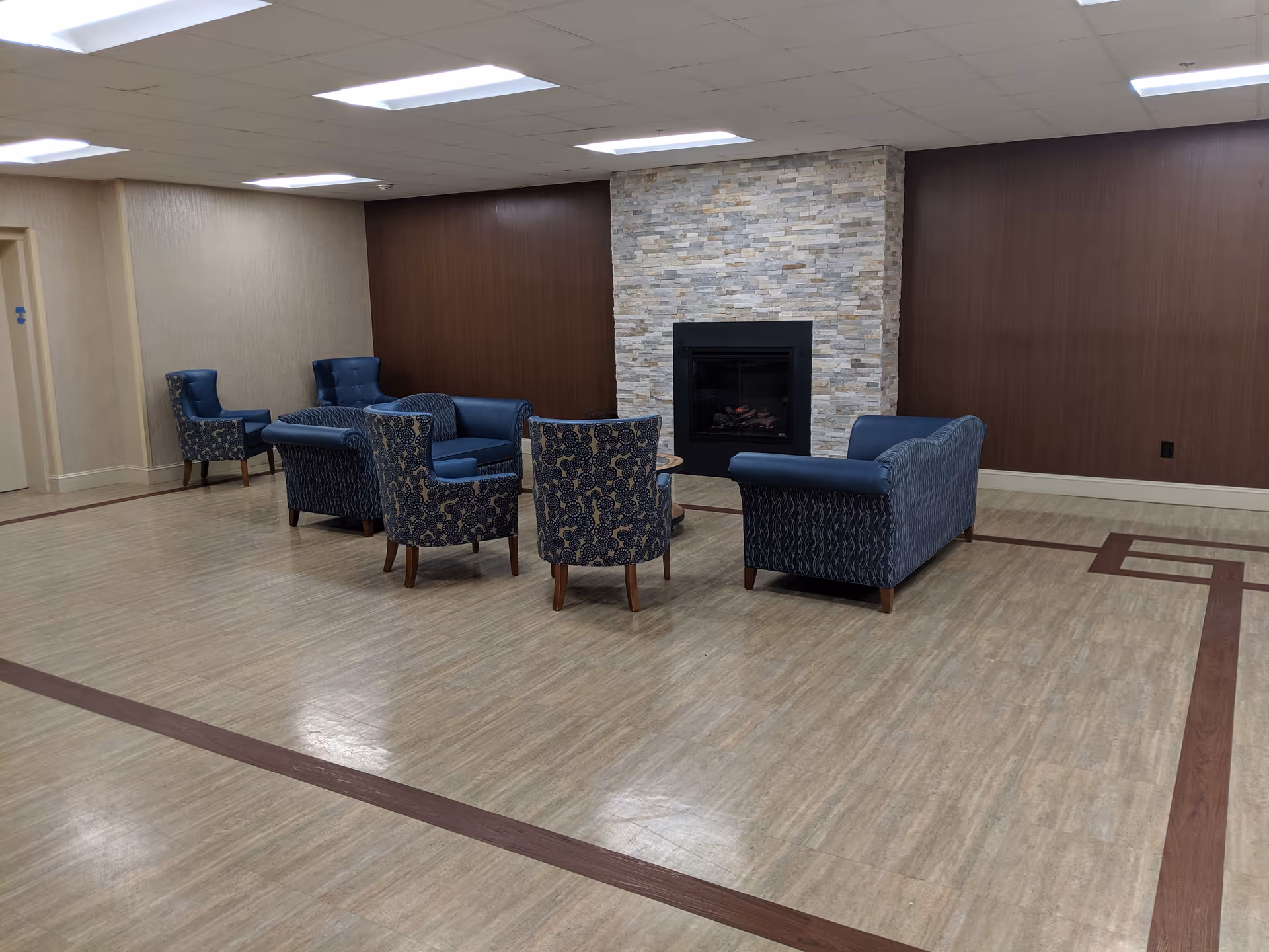 A spacious lobby with blue upholstered chairs arranged around a stone fireplace.