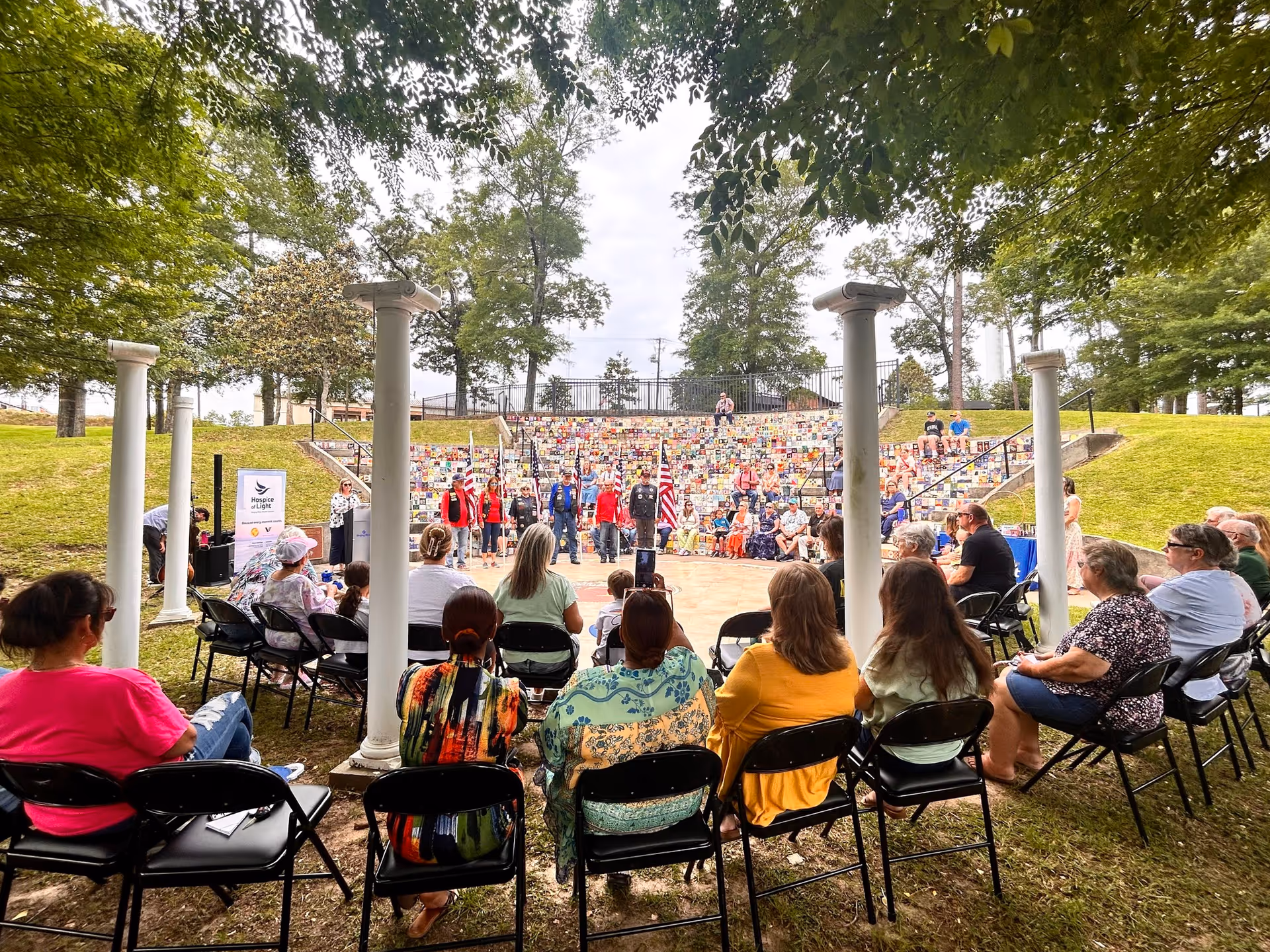 Outdoor audience seated in an amphitheater watches a group perform.