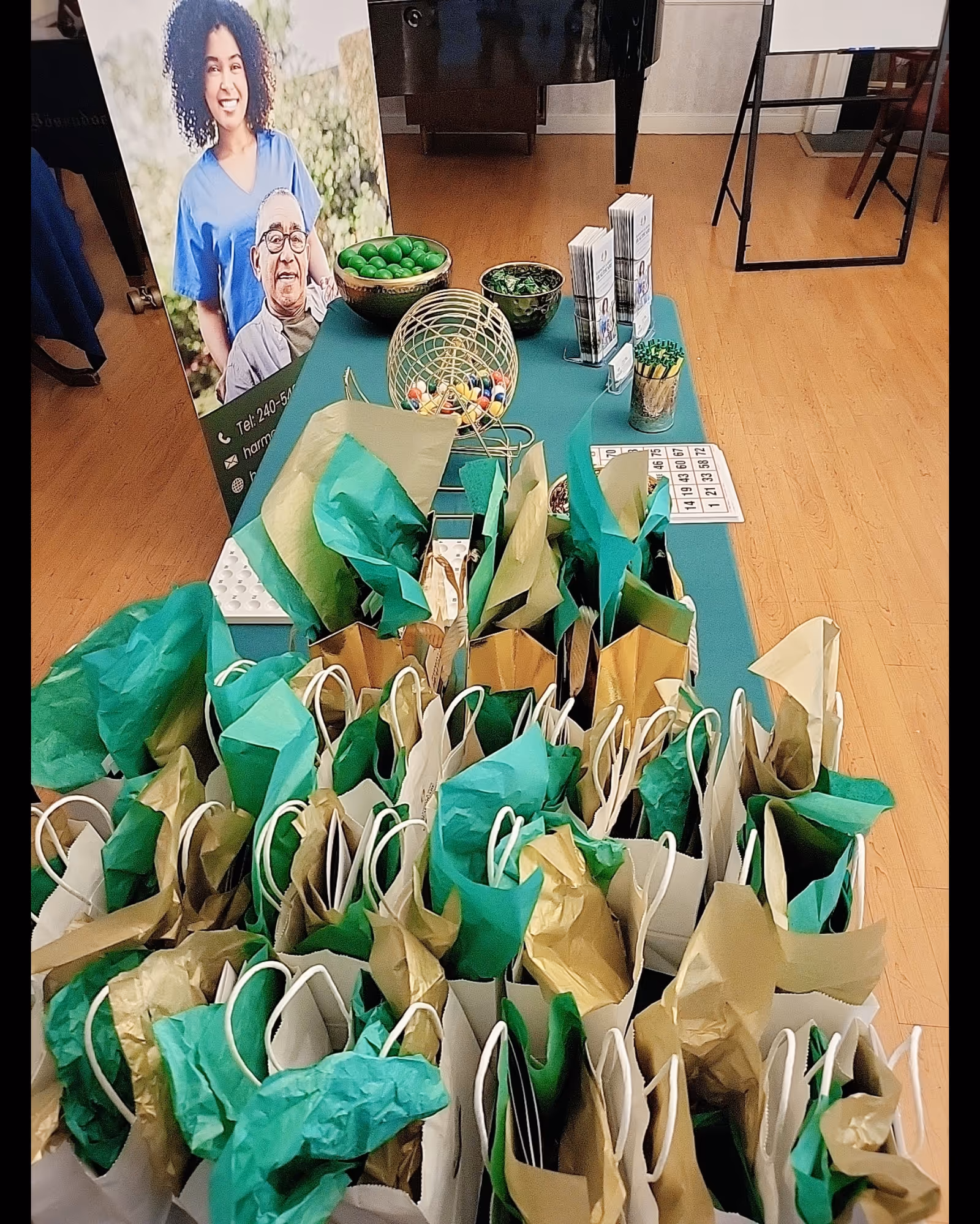 Inside a facility, green and gold gift bags fill a table beside a staff banner.