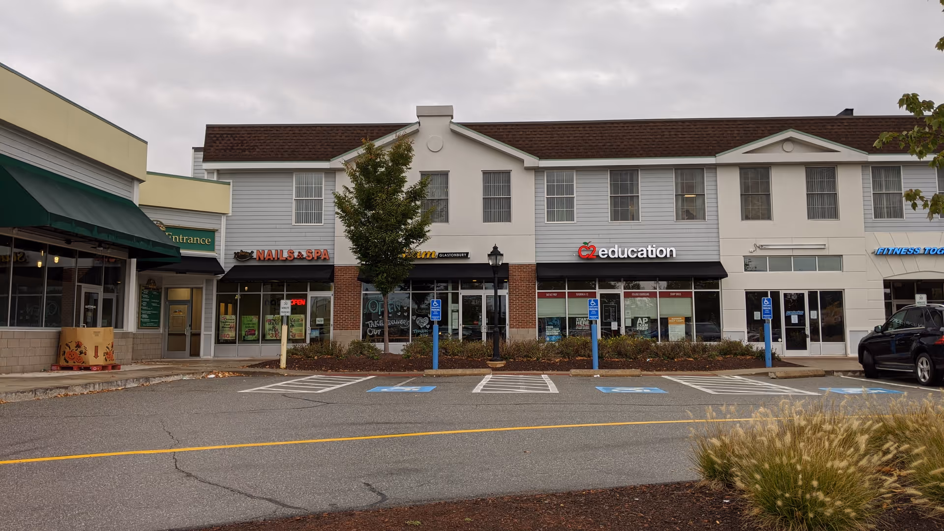 Exterior of a strip mall with multiple storefronts and a front parking lot.