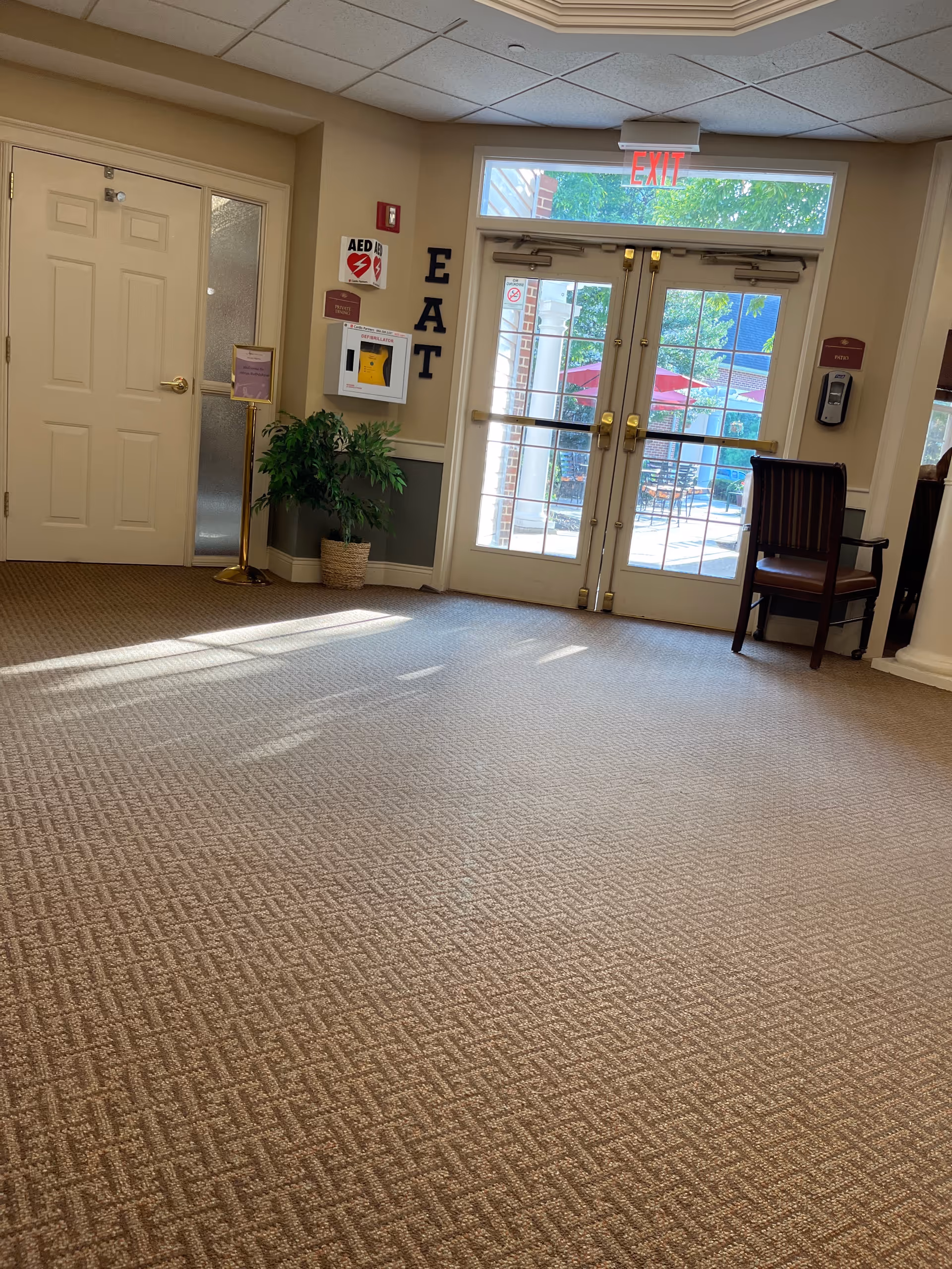 Lobby area with glass doors, exit sign, and a potted plant inside a senior living facility.