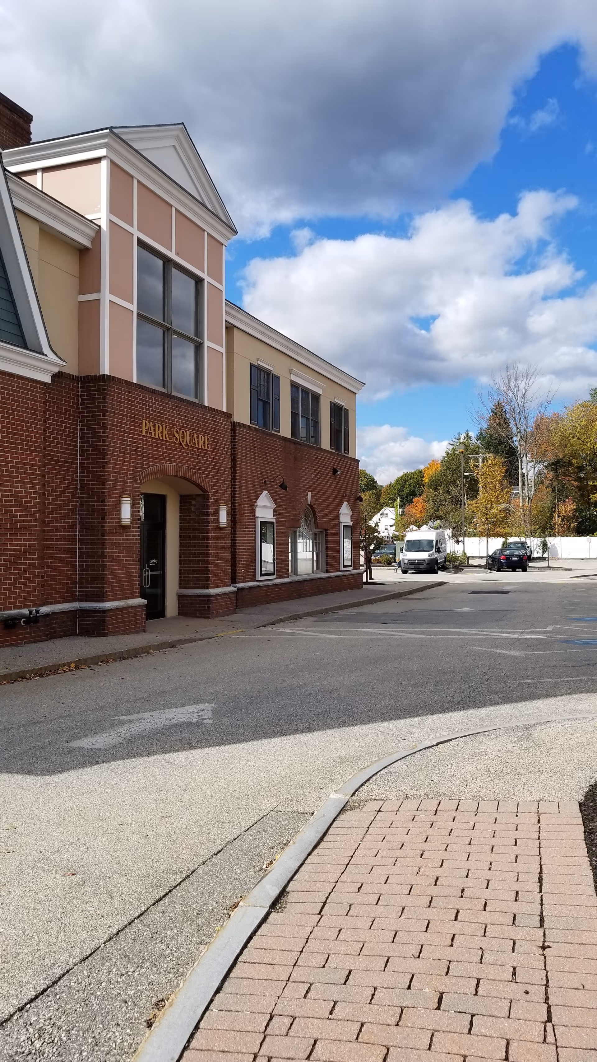 Exterior view of a brick senior facility with entrance, parked vehicles, and blue sky.