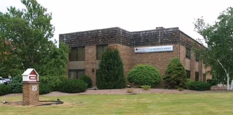 Brick building with trimmed shrubs and a front sign in a grassy, landscaped lot.
