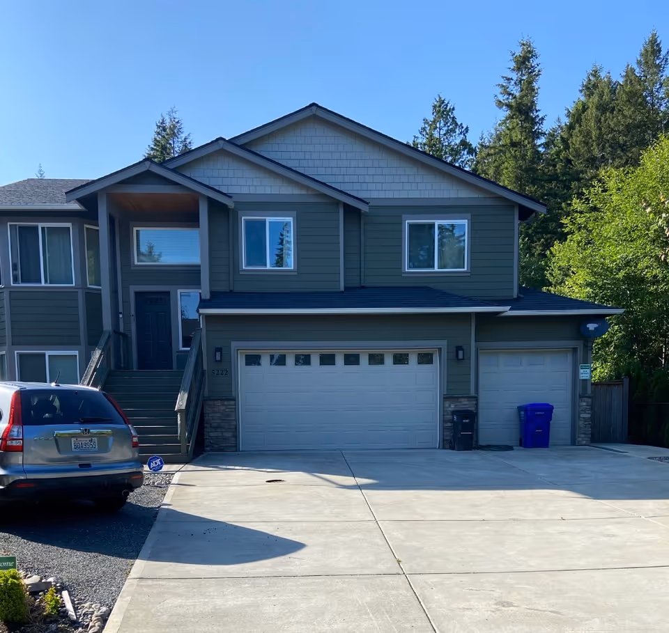 Two-story green townhouse-style building with multiple garage doors and a parked SUV.