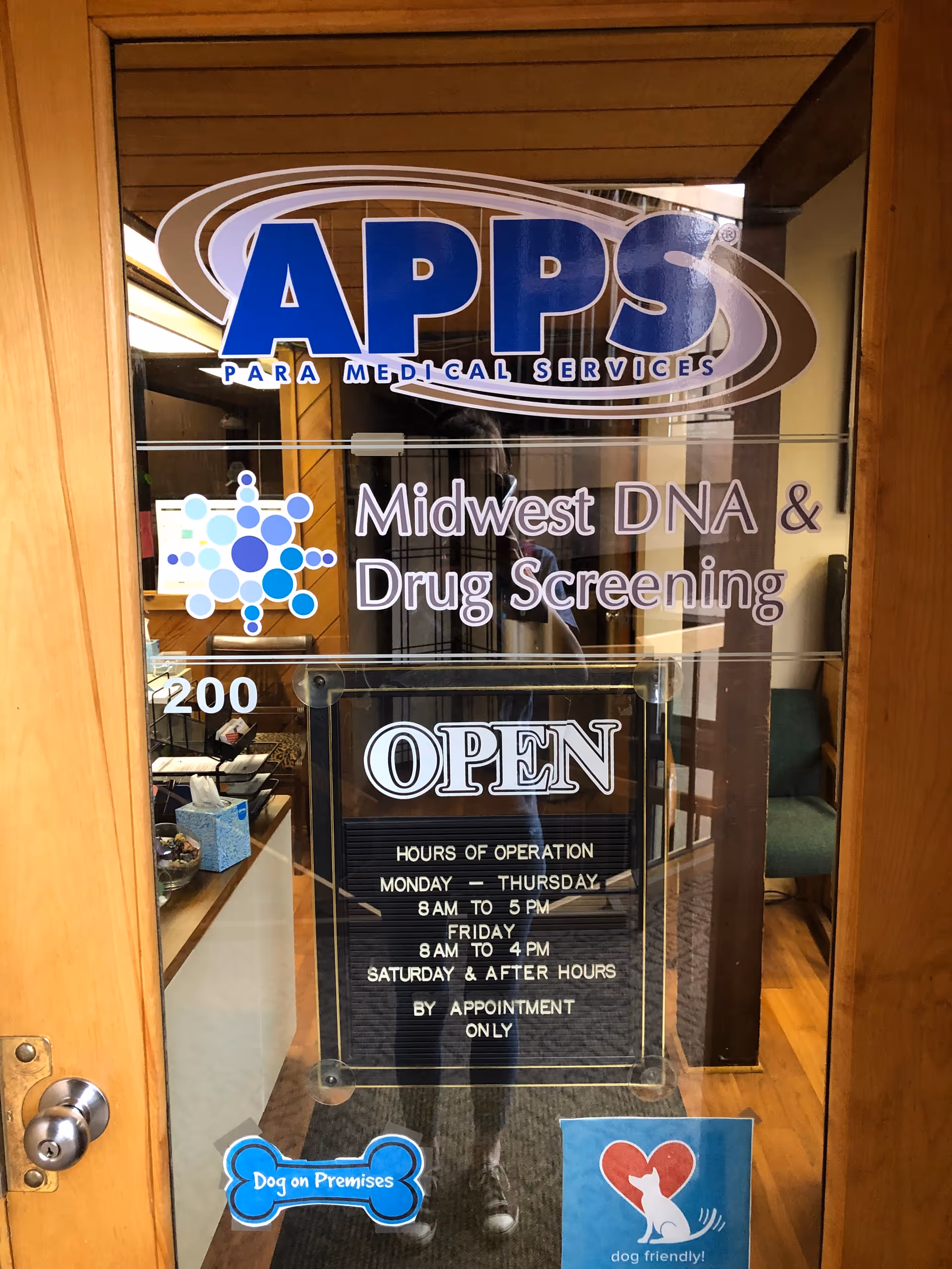 Glass door shows APPS Paramedical Services sign, Midwest DNA & Drug Screening, and open hours.