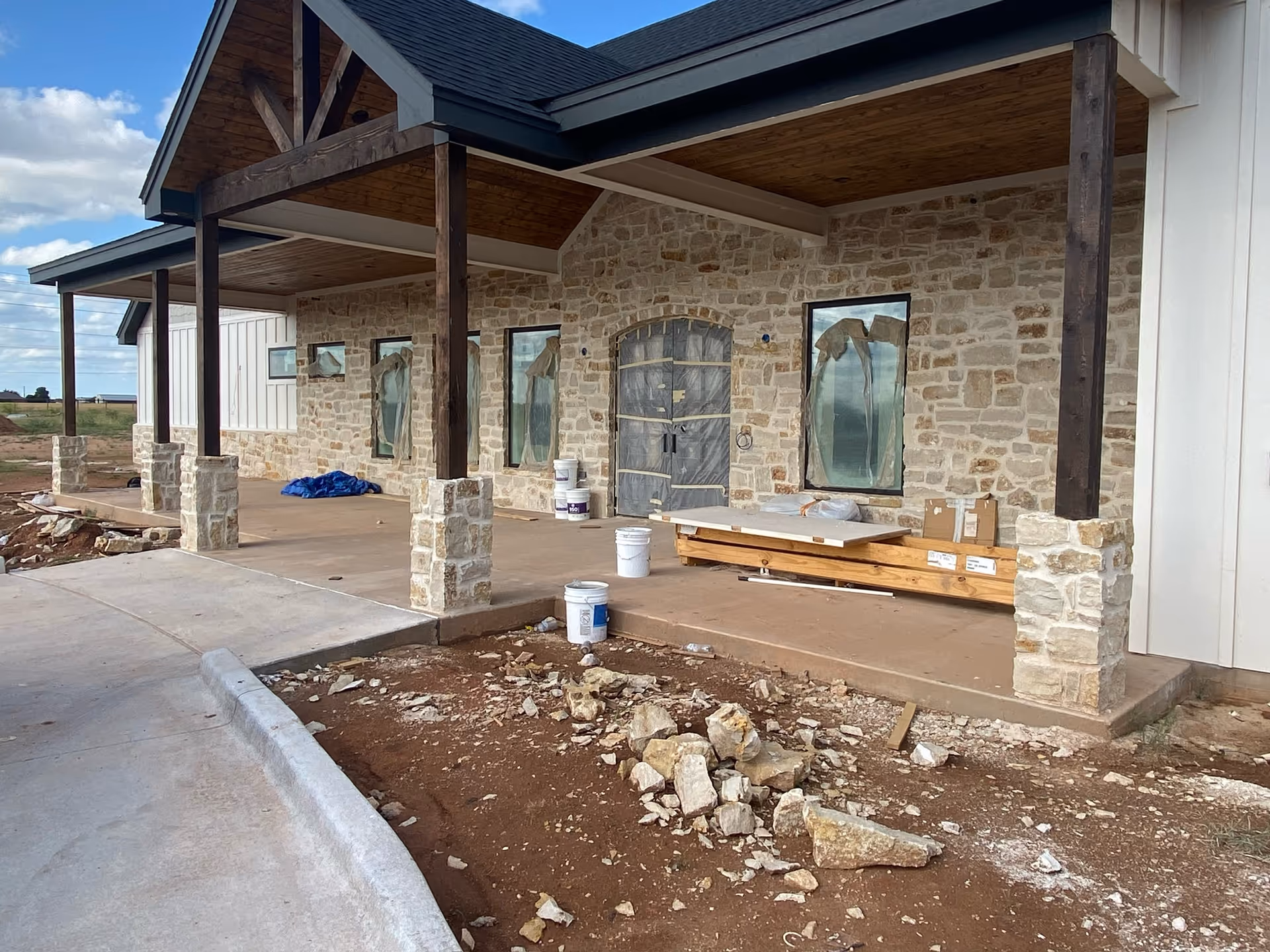 Stone-clad building front under construction with a covered porch and scattered materials.