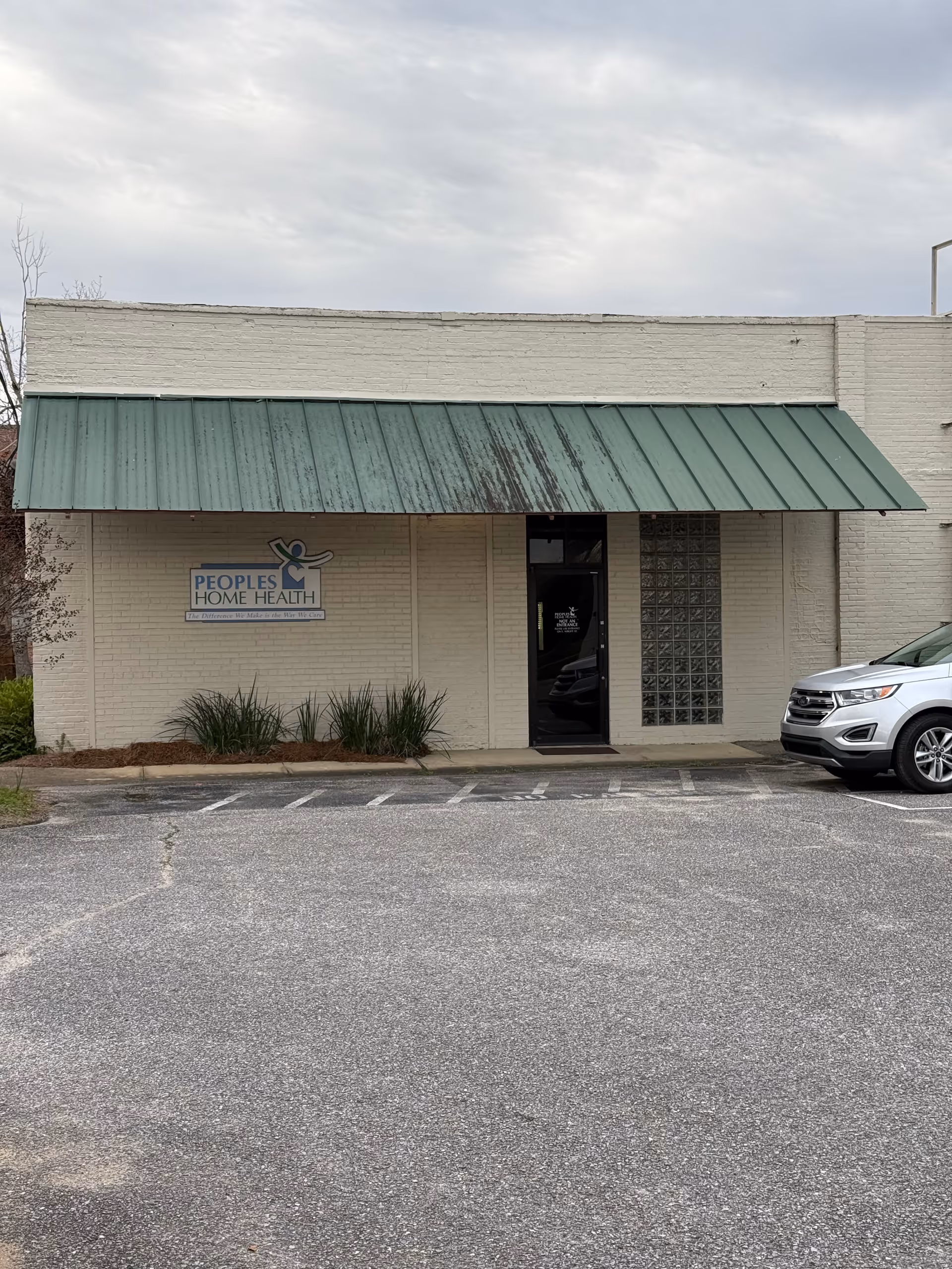 Brick building front with green metal awning, glass door, and parked vehicle.