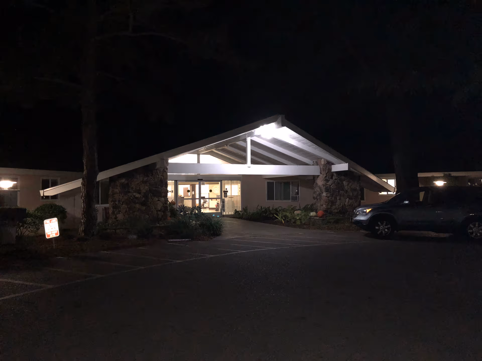 Night view of Cupertino Healthcare & Wellness entrance with illuminated doorway and parked car.