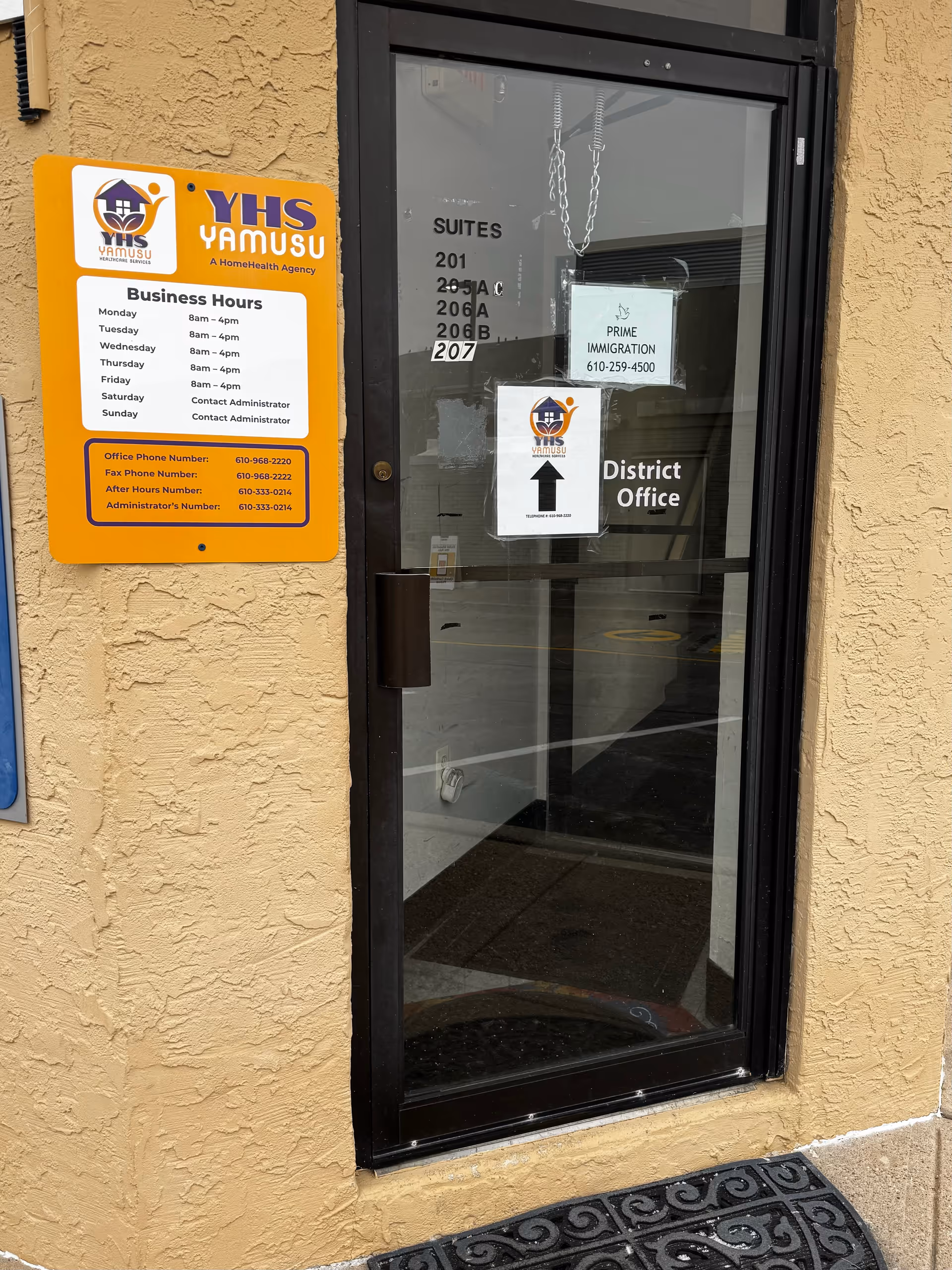 Exterior view of YaMusu Healthcare Services entrance with glass door and yellow sign.