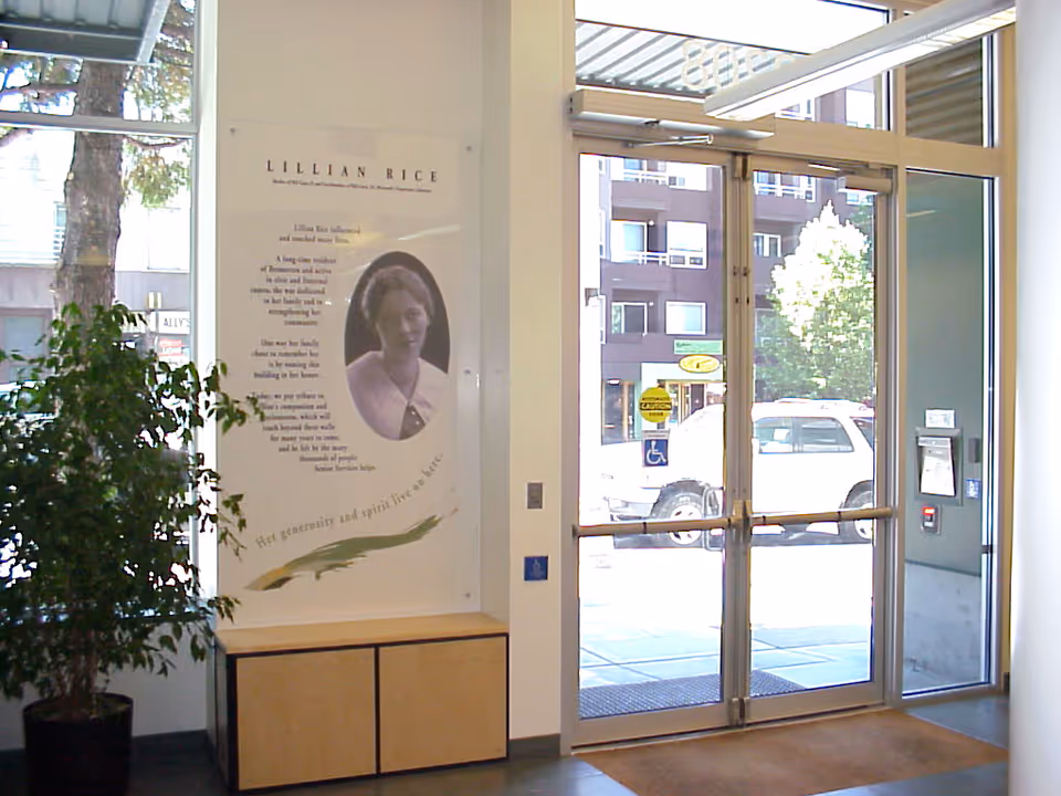 Lobby entrance with glass doors, a poster on the wall, and a plant near a bench.