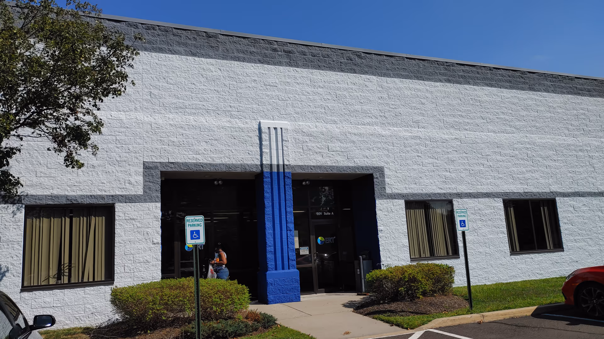 White brick building exterior with a blue entrance column and landscaping.