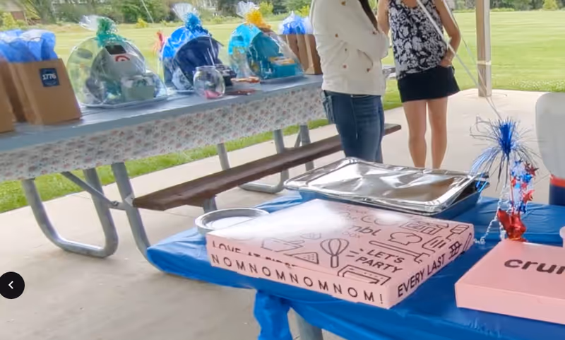 Outdoor pavilion with a table of gifts and people nearby during a celebration.