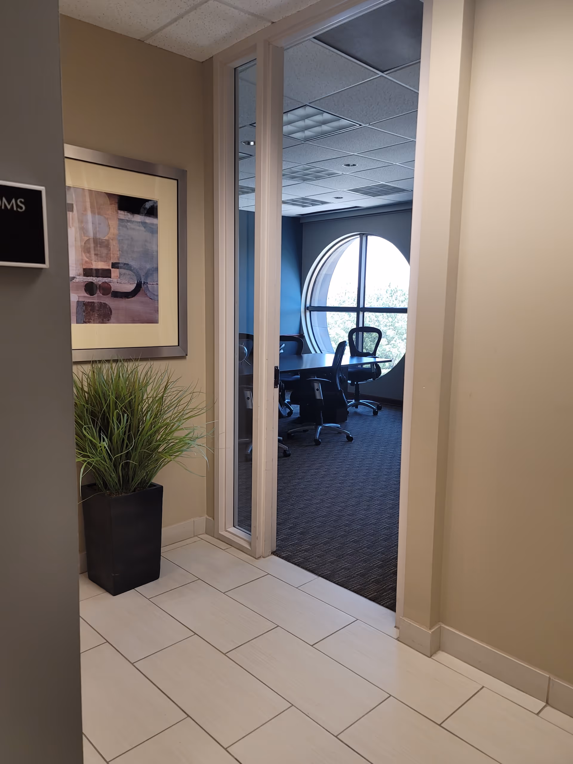 Hallway leading to a small office meeting room with chairs around a table and circular window.