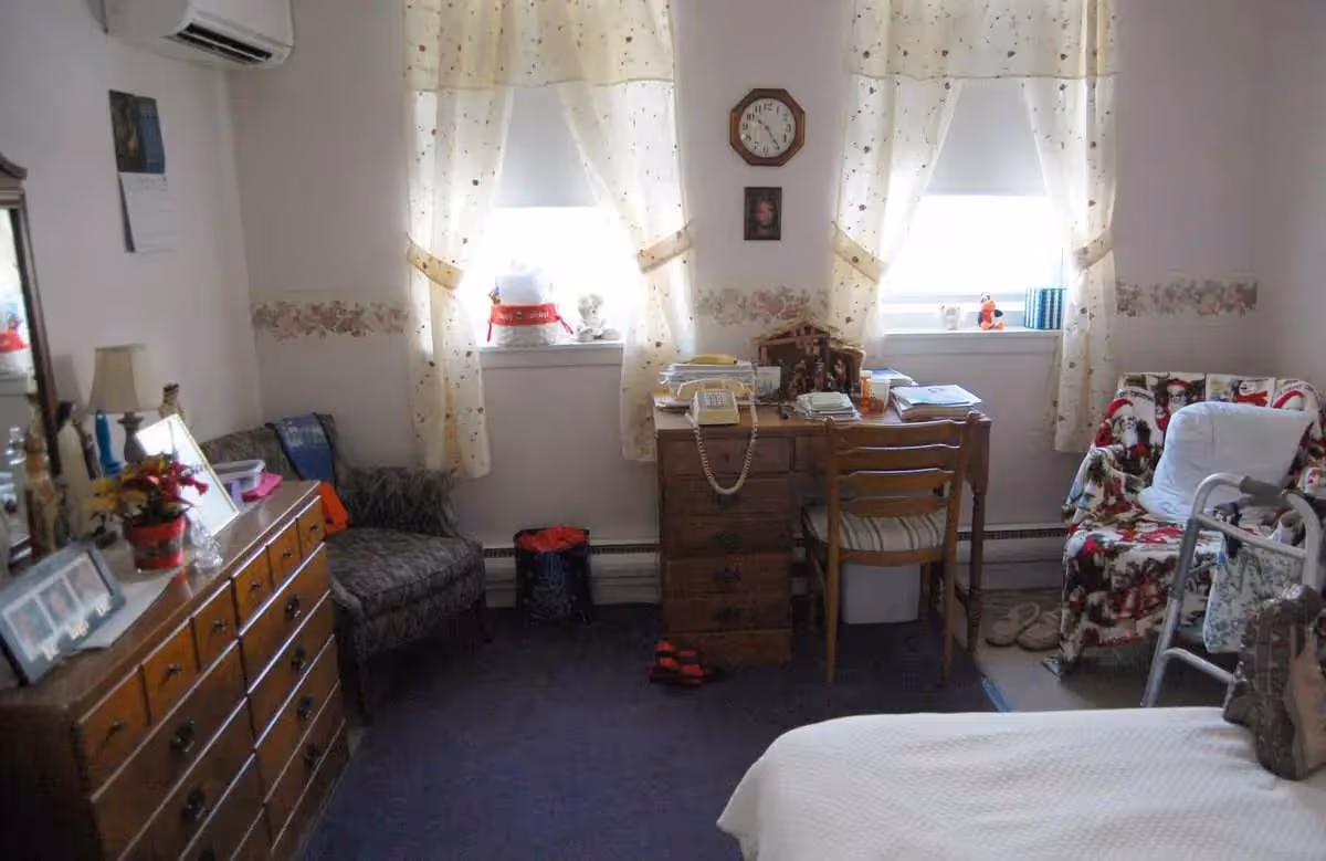 Cozy senior living room with a dresser, desk, chair, bed, and floral upholstery.