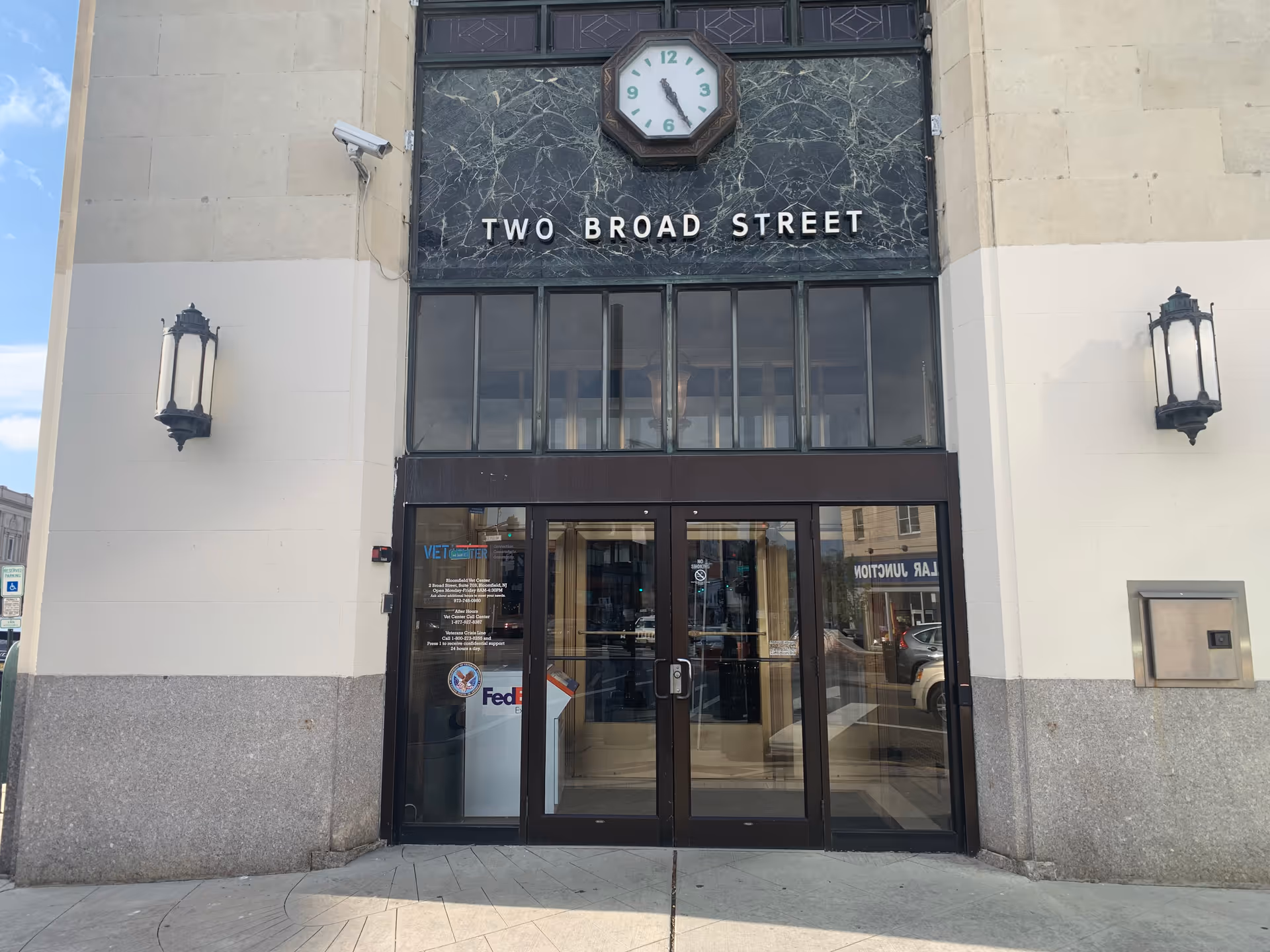 Facade of a building entry with a clock, glass doors, and Two Broad Street sign
