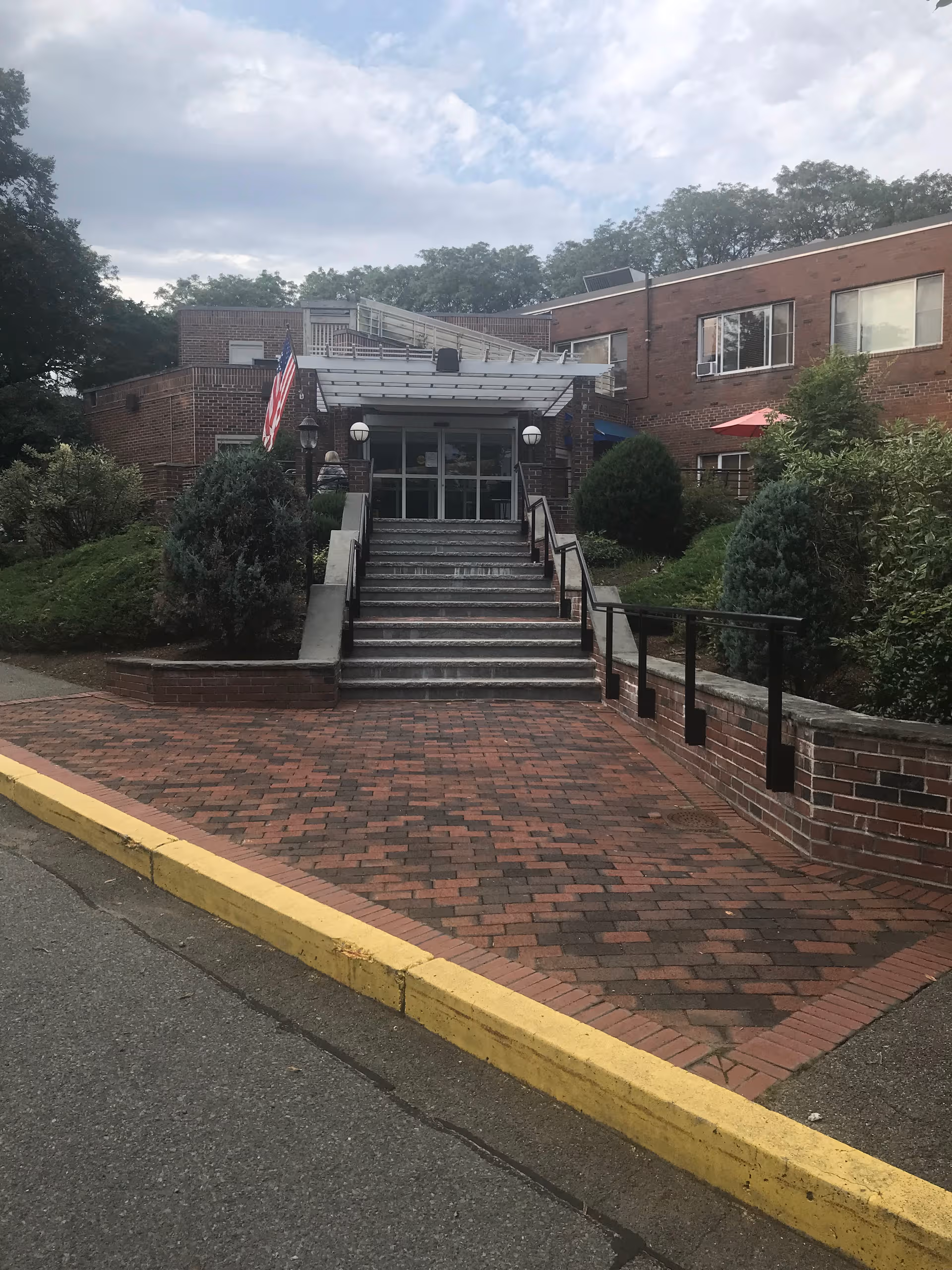 Saugus Rehabilitation & Nursing Center exterior with brick entrance, stairs, ramp, and flag.