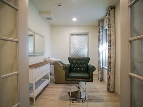 Interior of a senior living facility room with a green tufted chair and a sink counter.