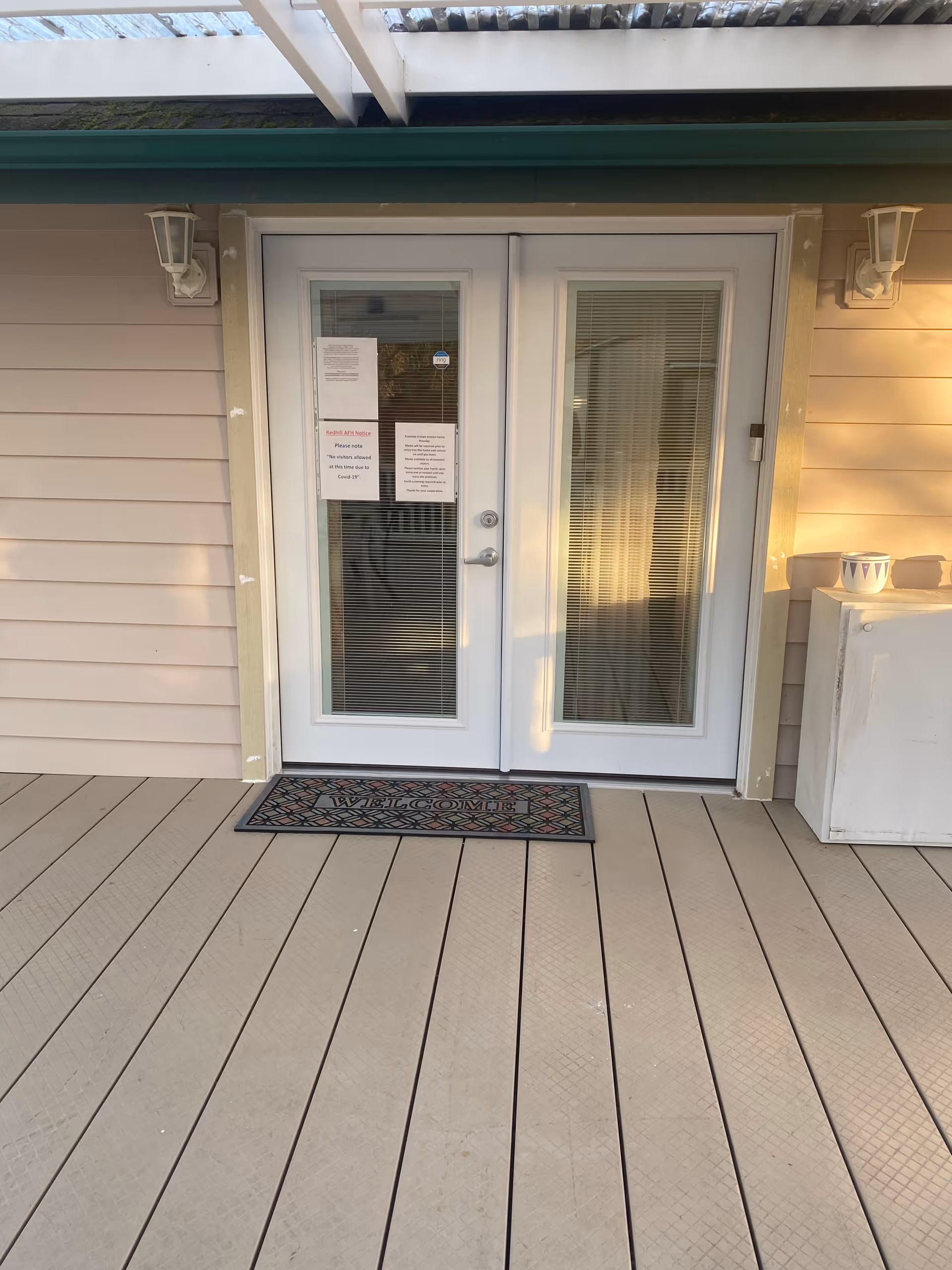 Double glass doors of a facility entrance with a welcome mat and beige siding.