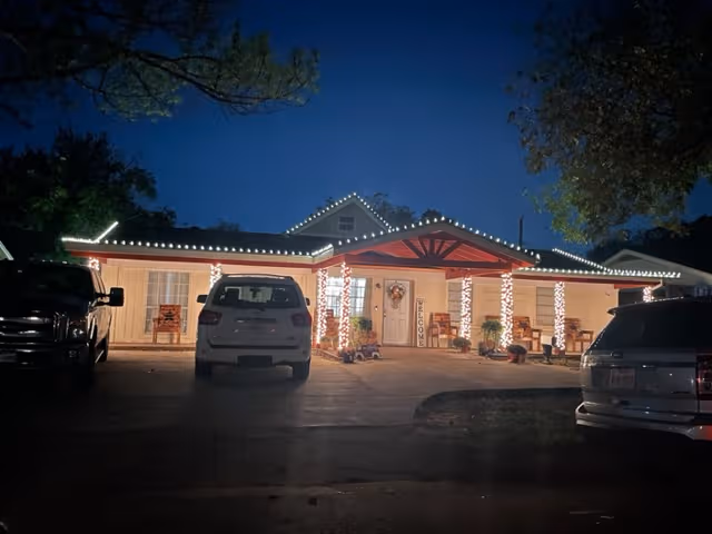 Night exterior of Love and Care Senior Services building with string lights and parked cars
