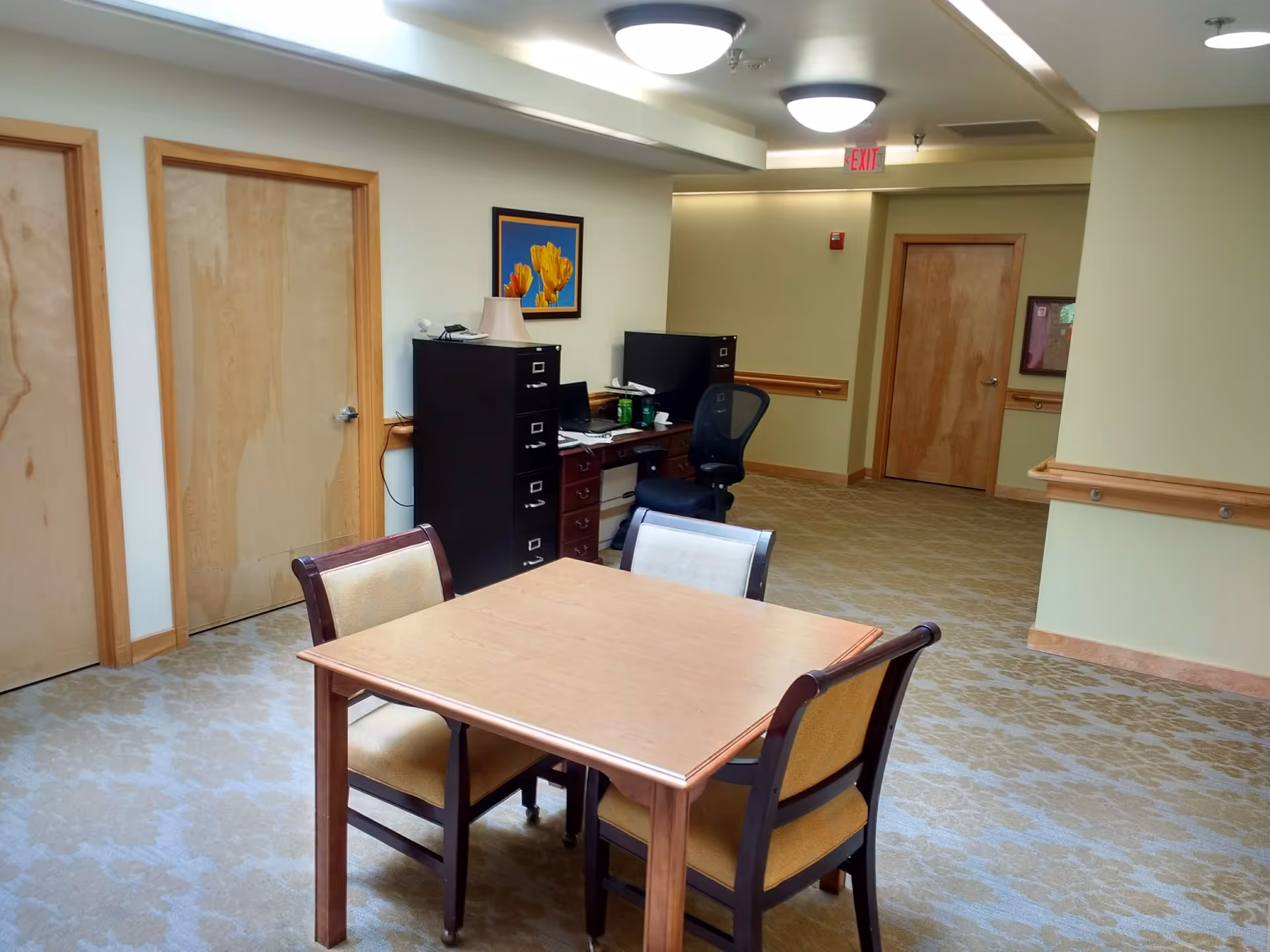 Indoor communal lounge with a wooden table, four chairs, and office area.