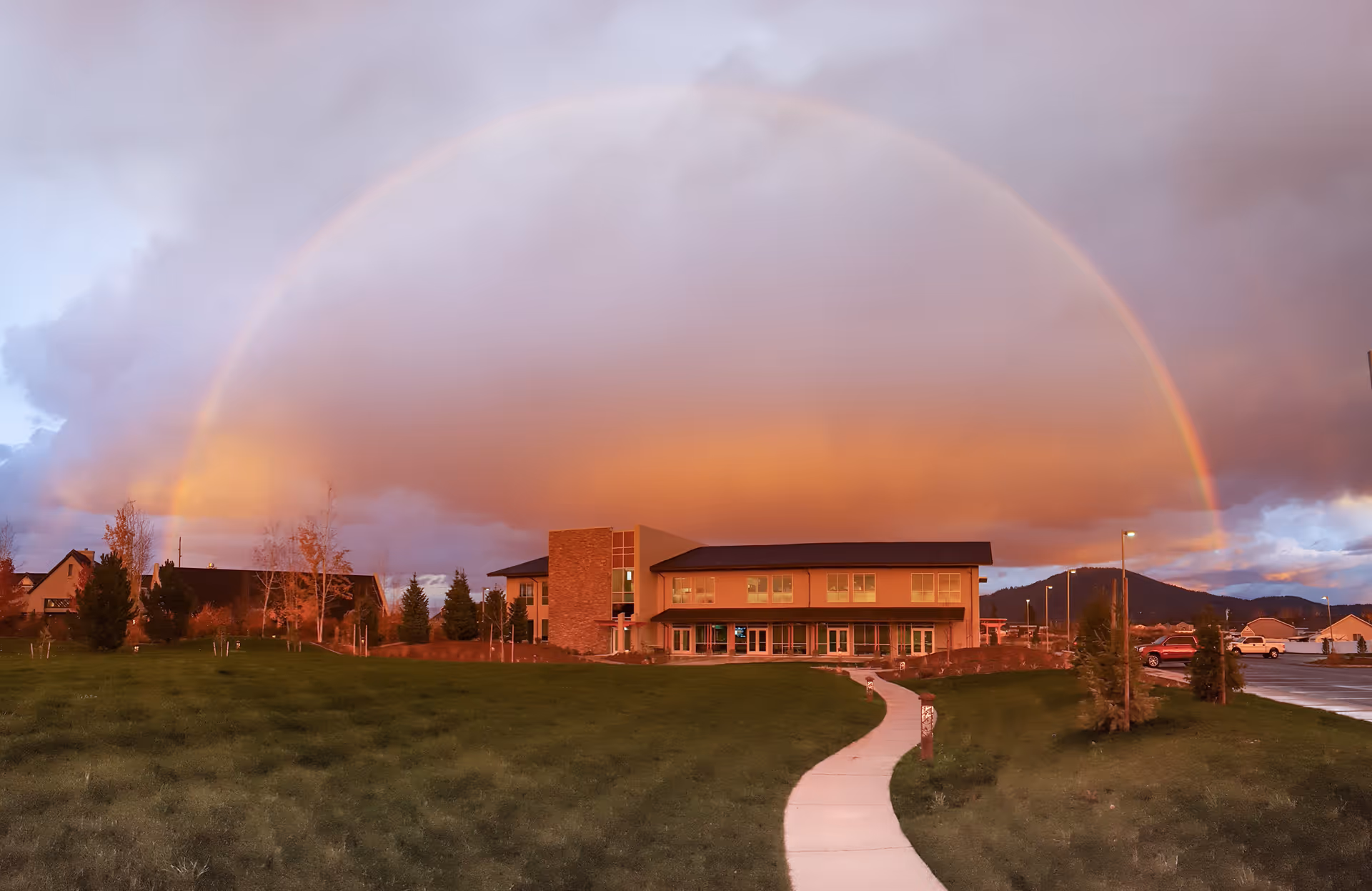 Exterior view of Hospice of North Idaho with a rainbow arching over the building and path.