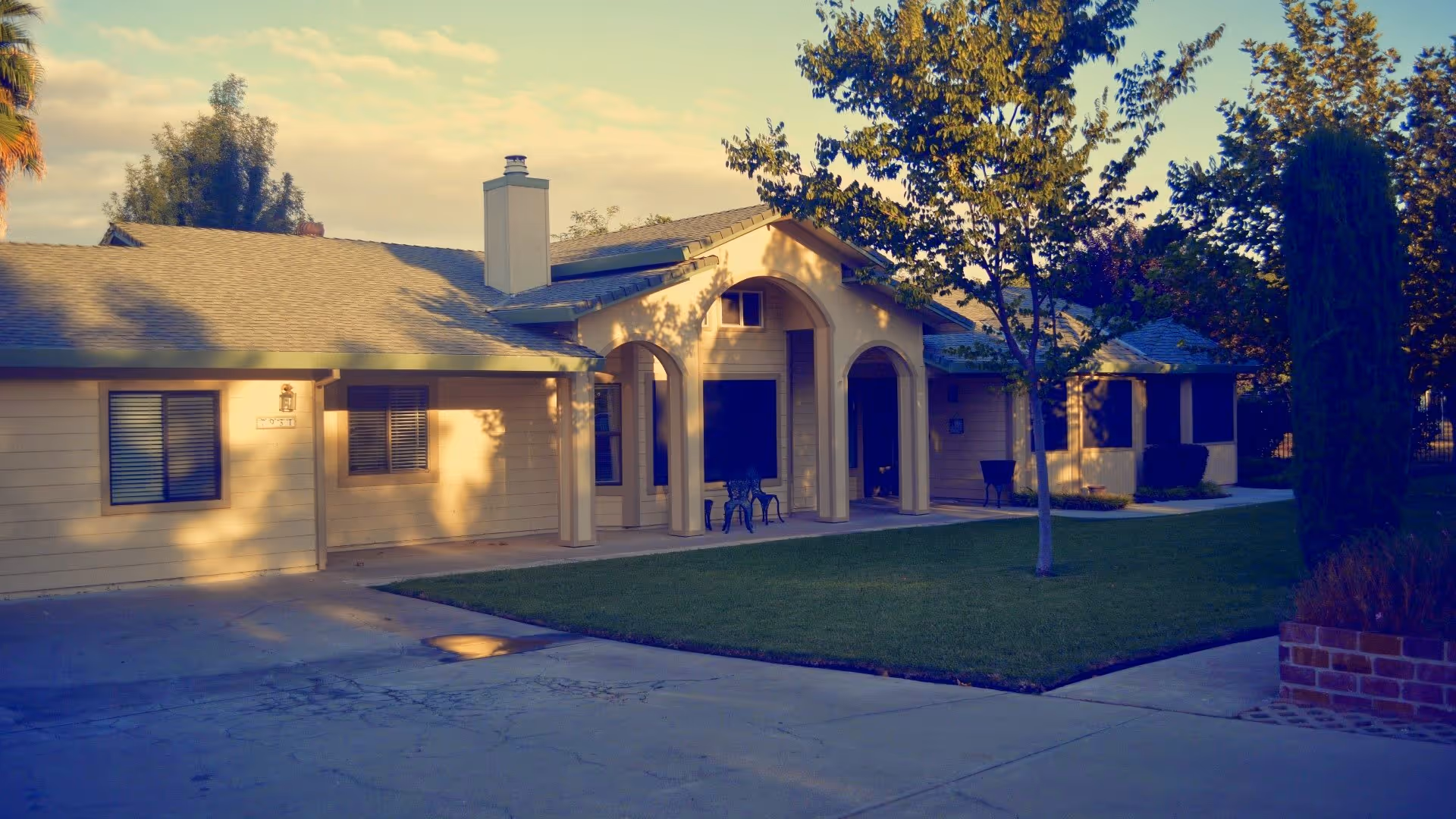 Exterior of a single-story senior living facility with arches, lawn, and driveway.