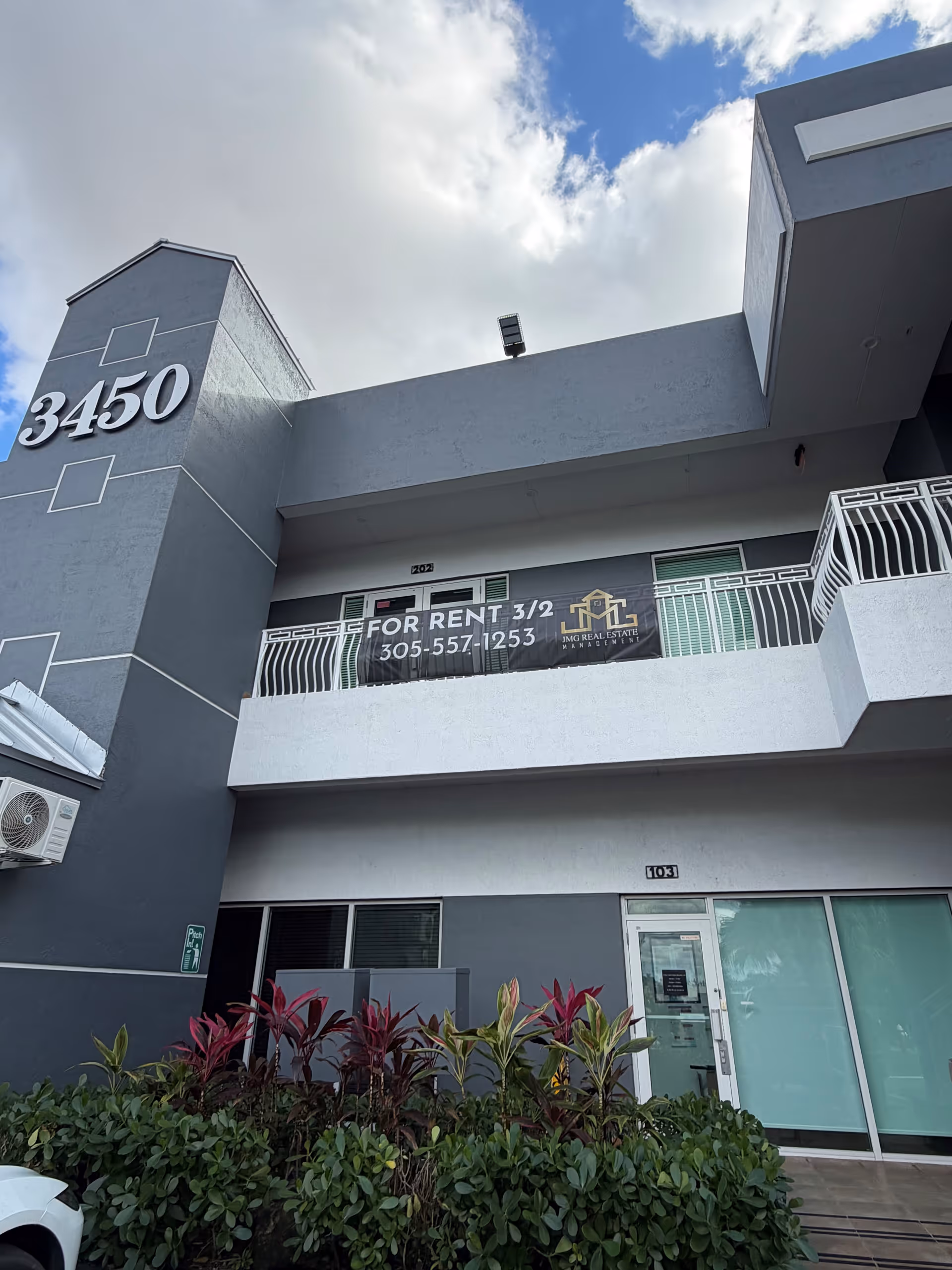 Exterior view of a gray, multi-story building with a for-rent banner and storefront windows.