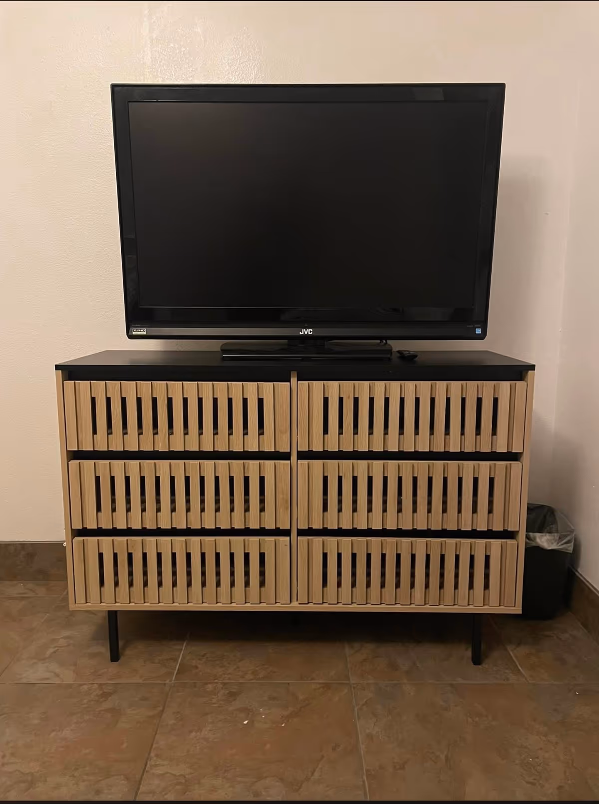 TV on a wooden slatted cabinet in a plain tiled room.