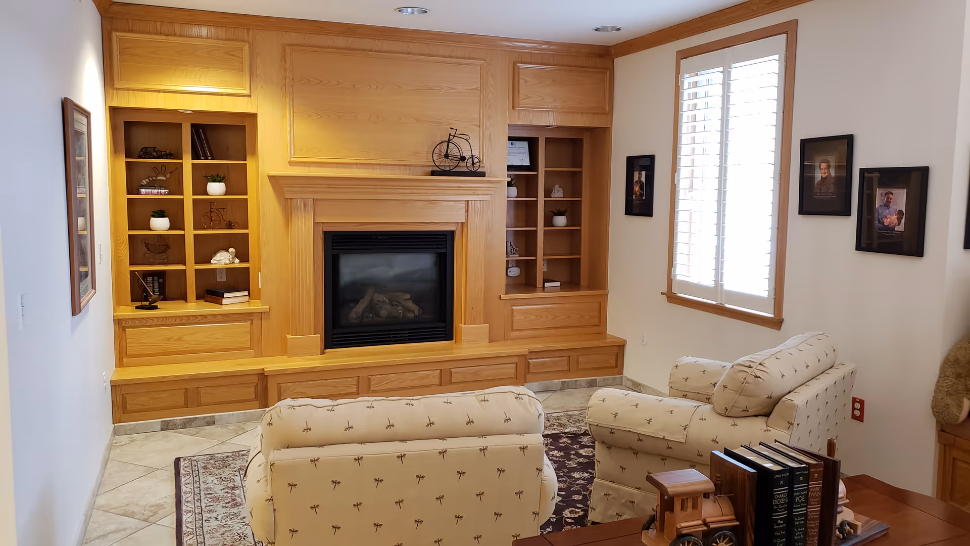 A cozy living room with built-in wooden shelves, fireplace, and patterned cream chairs.