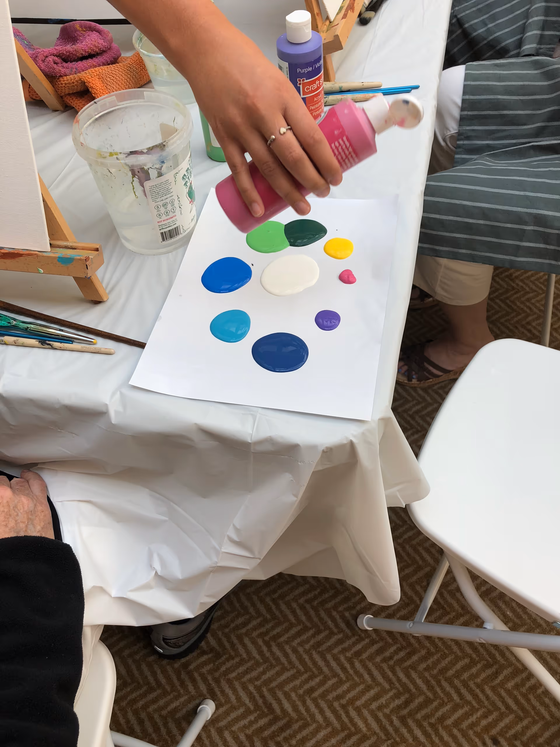 Hand applies colorful paint dots onto a sheet at a crafting table.
